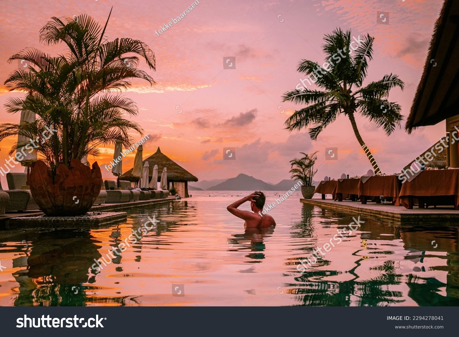 young men in a swimming pool during sunset, Luxury swimming pool in a tropical resort, relaxing holidays in Seychelles islands. La Digue, a Young guy during sunset by swim pool #2294278041