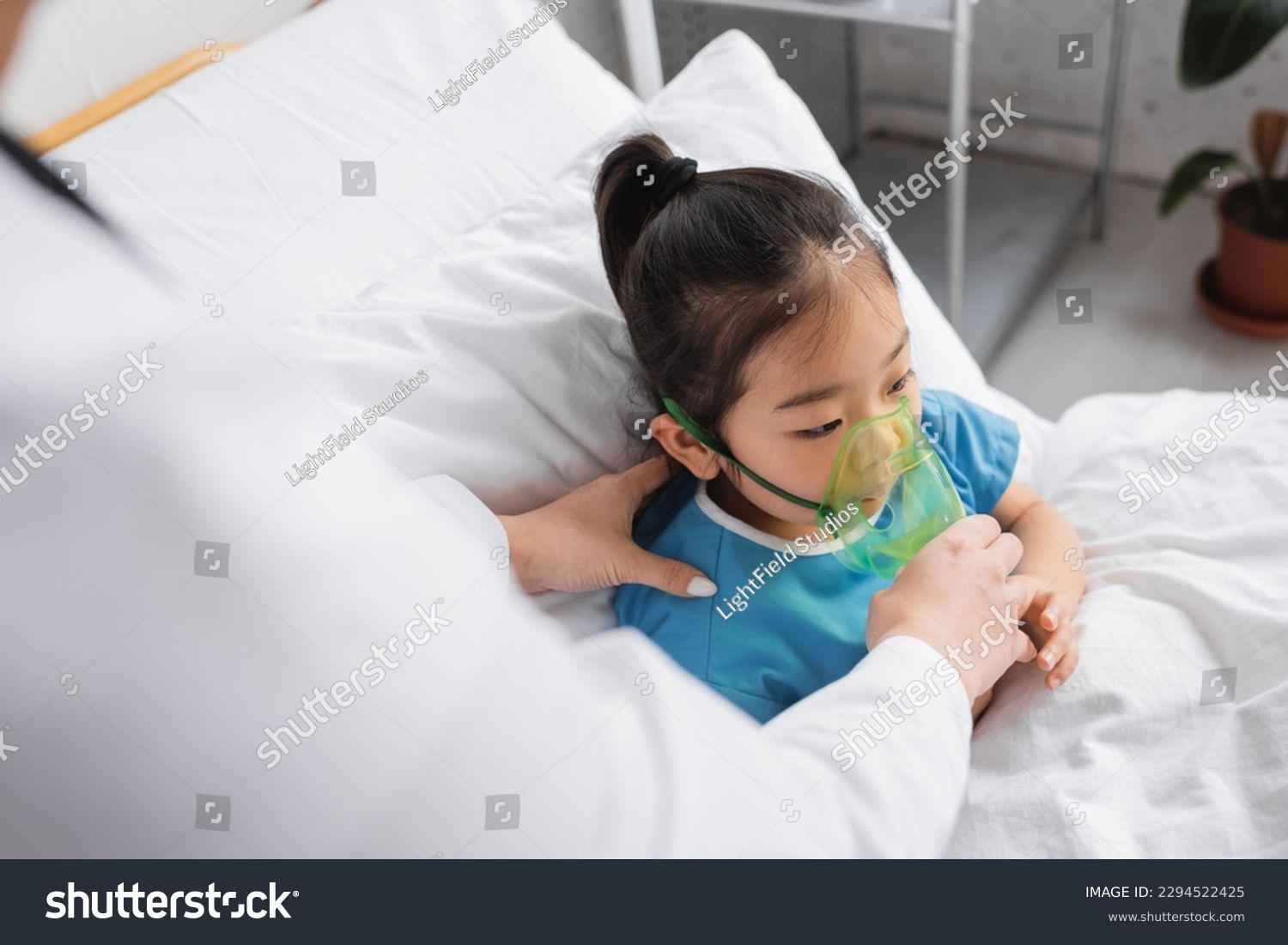 blurred doctor adjusting oxygen mask on sick asian child on hospital bed #2294522425