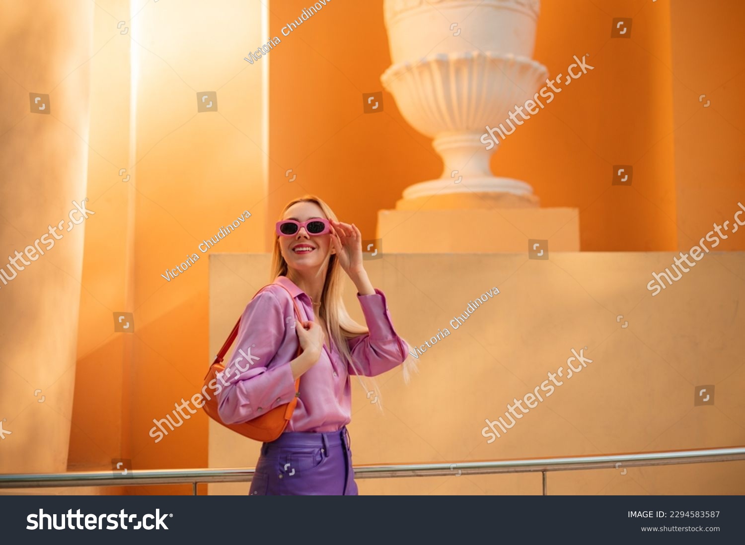 Fashionable happy smiling woman wearing trendy spring, summer outfit with pink sunglasses, satin blouse, purple trousers, orange color faux patent leather baguette bag. Copy, empty space for text #2294583587