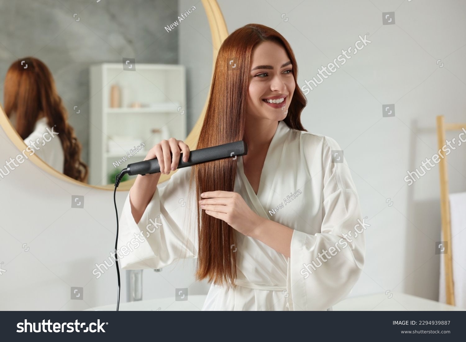 Beautiful woman using hair iron in room #2294939887