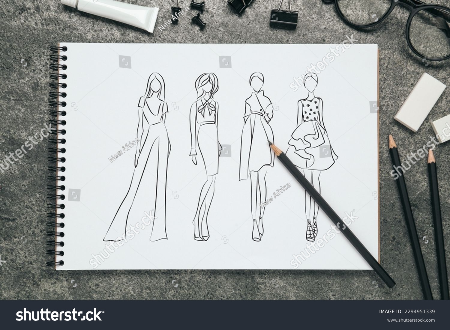 Sketches of different clothes in pad on grey textured table. Fashion designer's desk with stationery, flat lay #2294951339