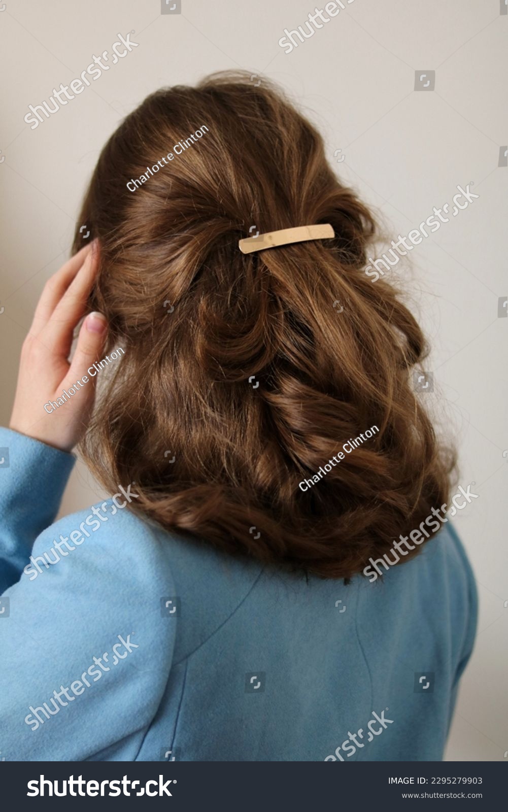 Young woman with thick, natural blonde hair pulled back and pinned half-up by a barrette hair clip. Gold metal barrette. Pretty hairstyle. Elegant hairstyle. Blue coat.  #2295279903