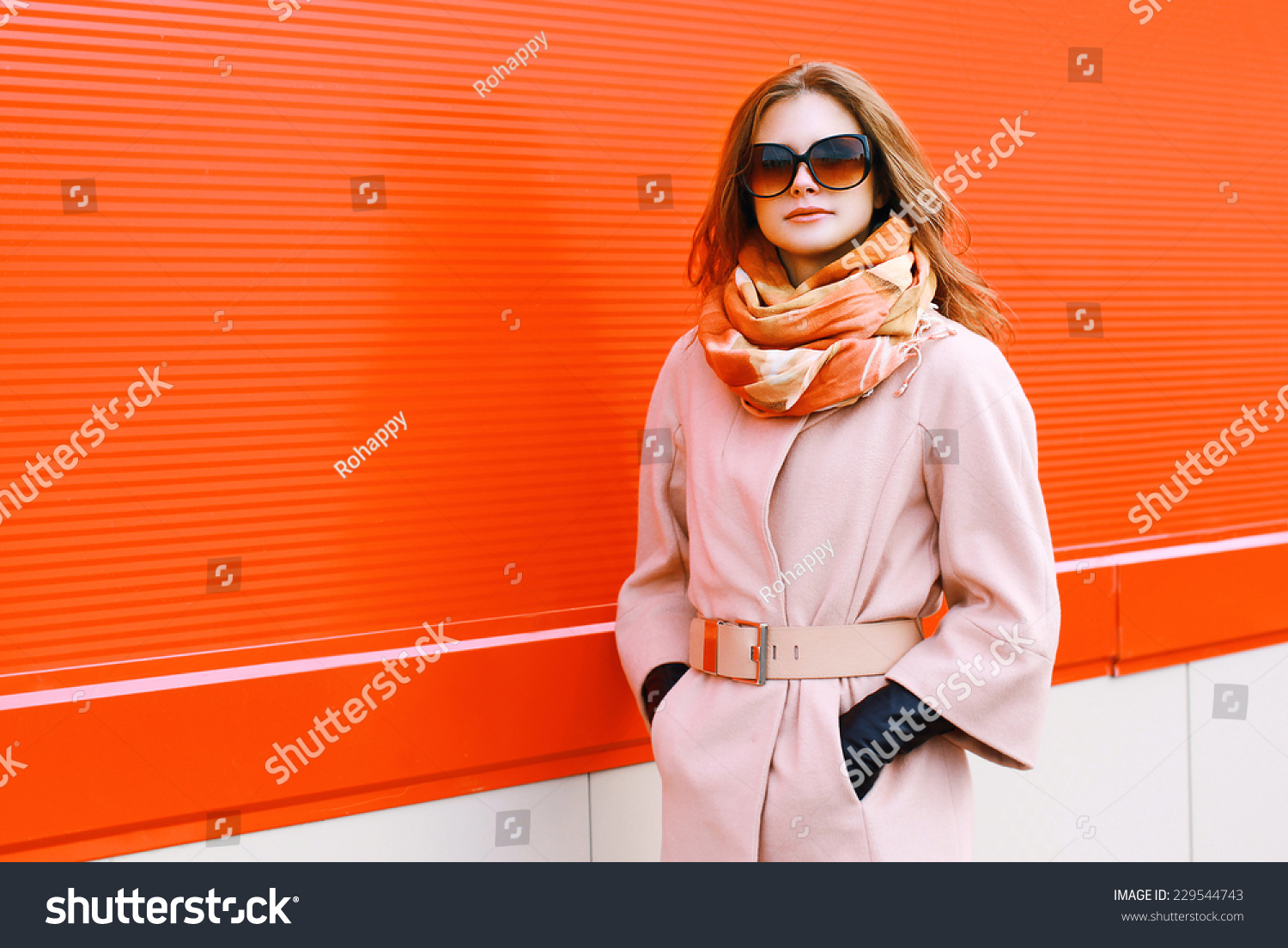 Beauty, fashion, shopping and people concept - pretty stylish woman in coat and sunglasses posing outdoors against colorful wall in the city #229544743