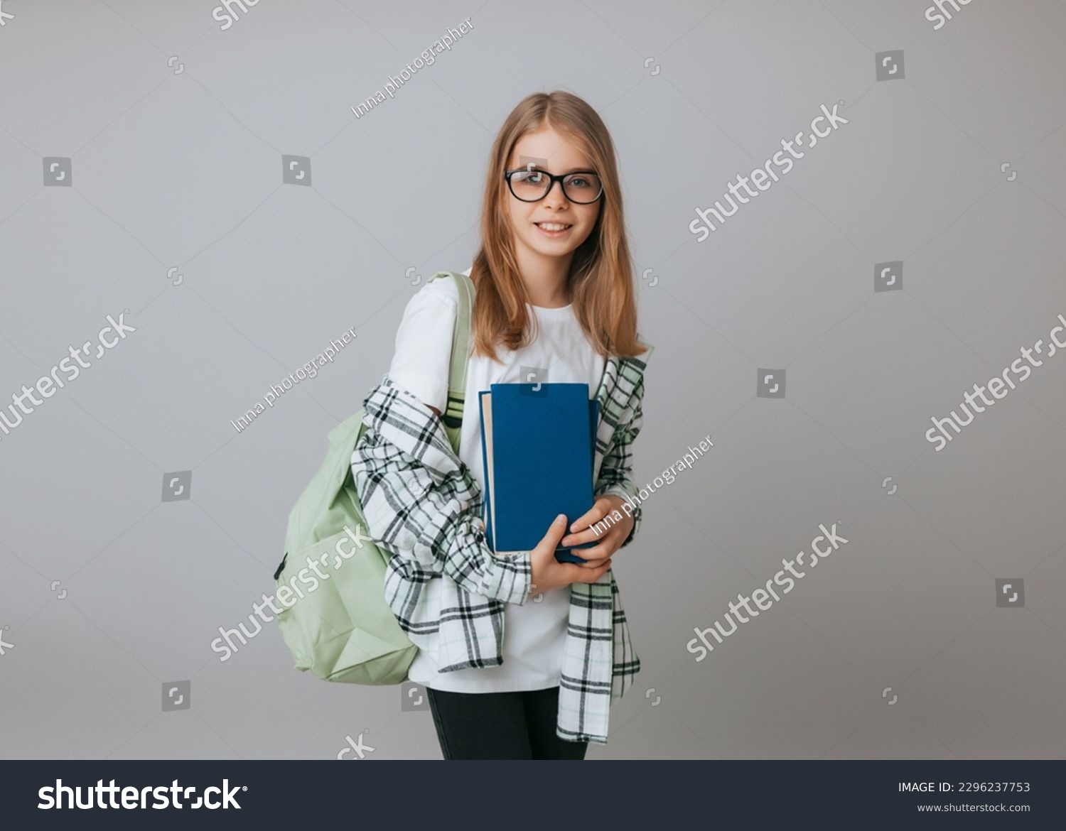 Smiling little schoolgirl 11-13 years old with backpack holding book isolated on gray background studio portrait. The concept of children's lifestyle. Education at school. #2296237753