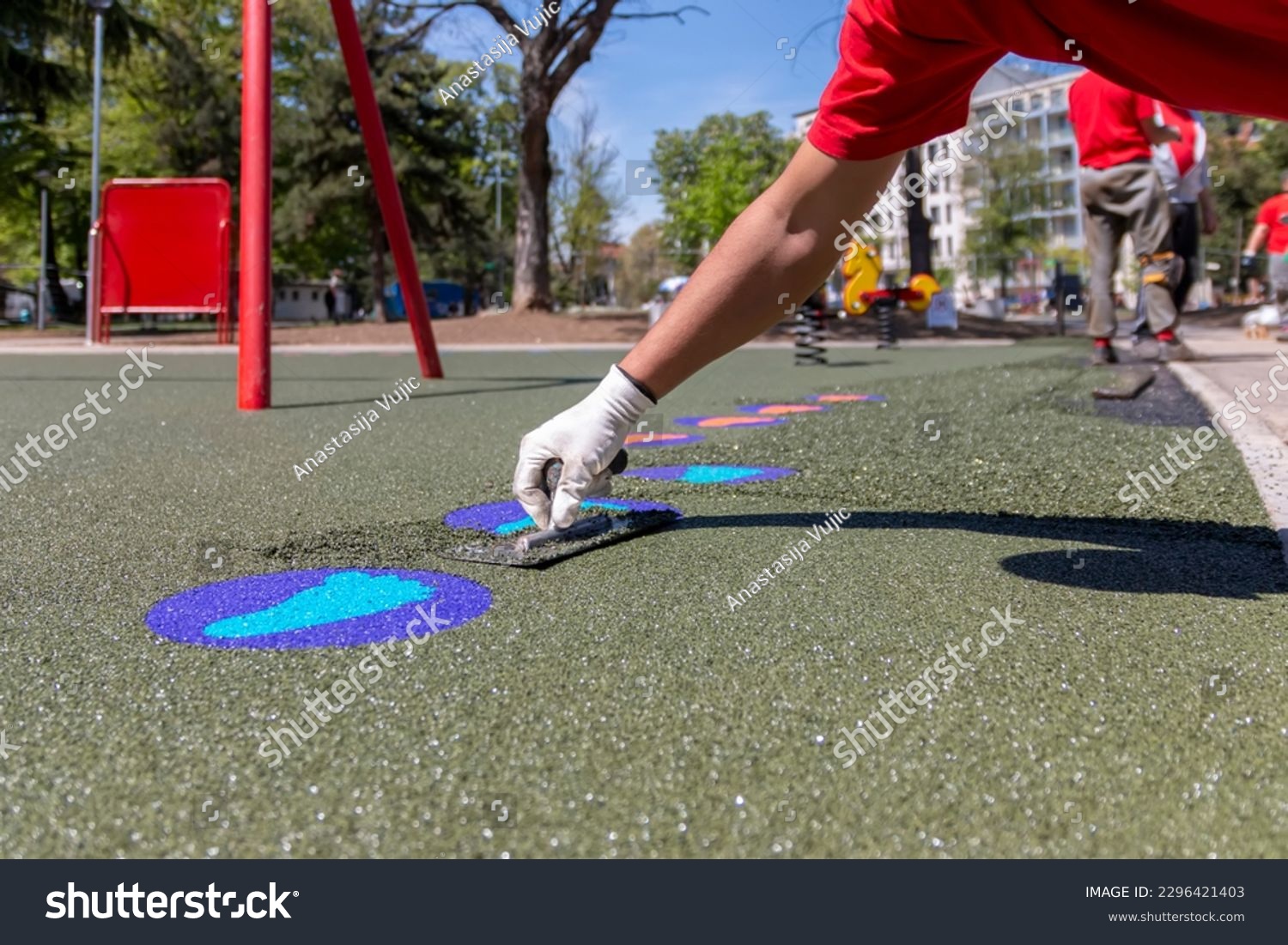 A mason hand with trowel  spreading and leveling soft rubber crumbs rubber mulch 
for children's playground. Outdoor soft coating and floor covering for sports. Rubber surface for safety. #2296421403