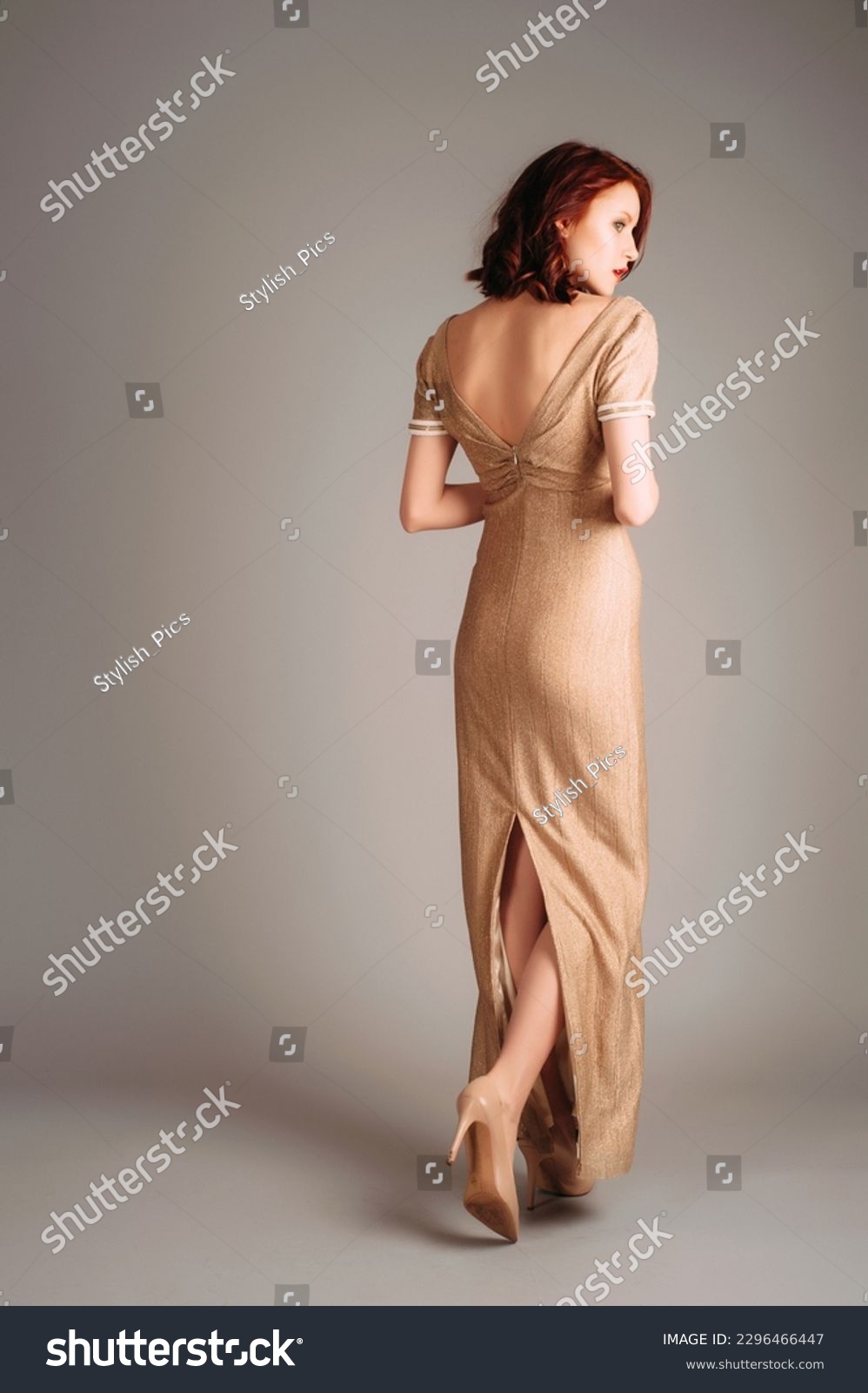 Ivory maxi dress with gold glitter, short sleeves and v line neckline. Beautiful tall red-haired young woman walking in slim backless evening gown and high heels. Total beige look. Rear view. #2296466447