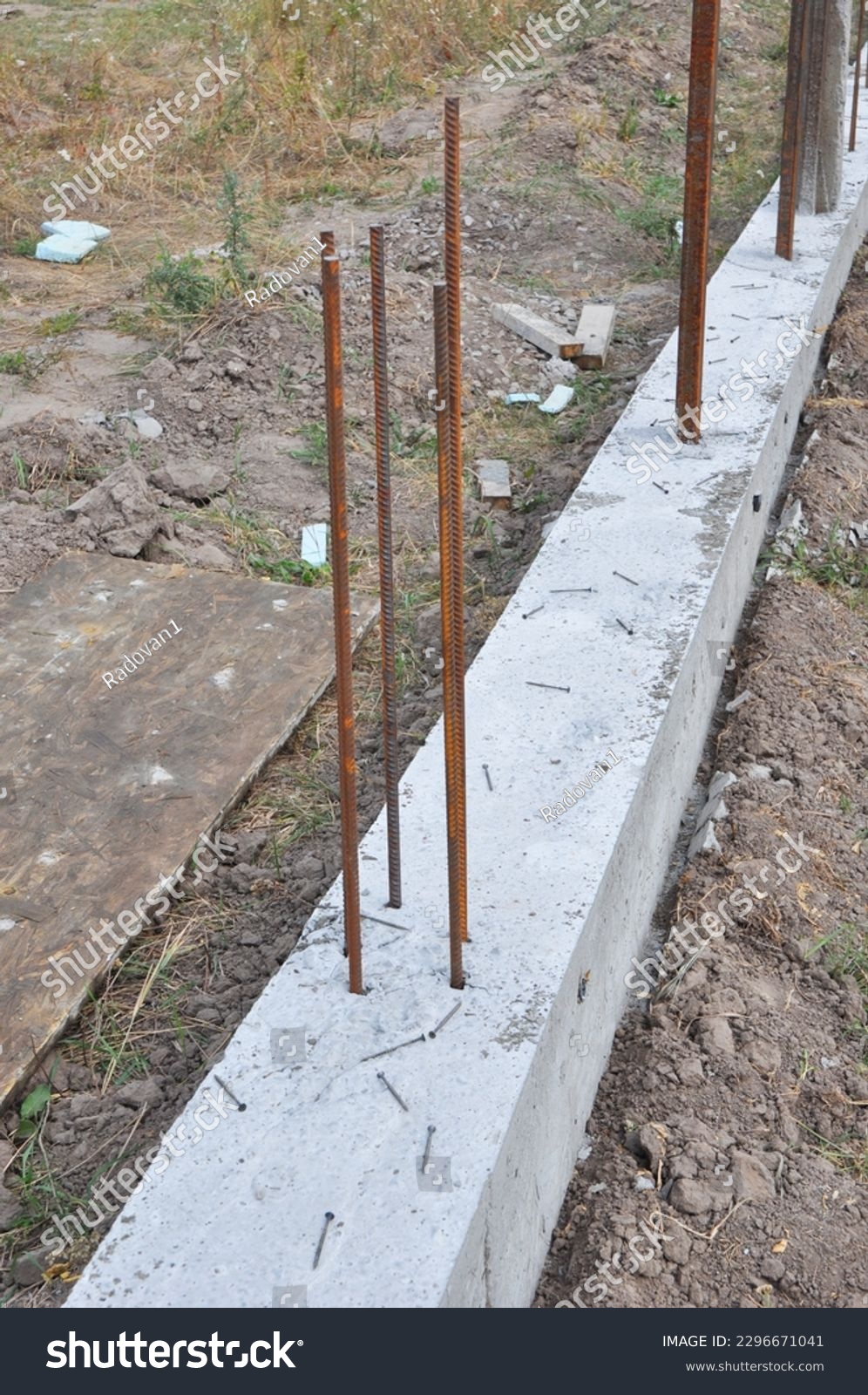 The concrete footer for new fence mounting. Fence footings. Close up on reinforced concrete footing for fence foundation with reinforcing bar. #2296671041