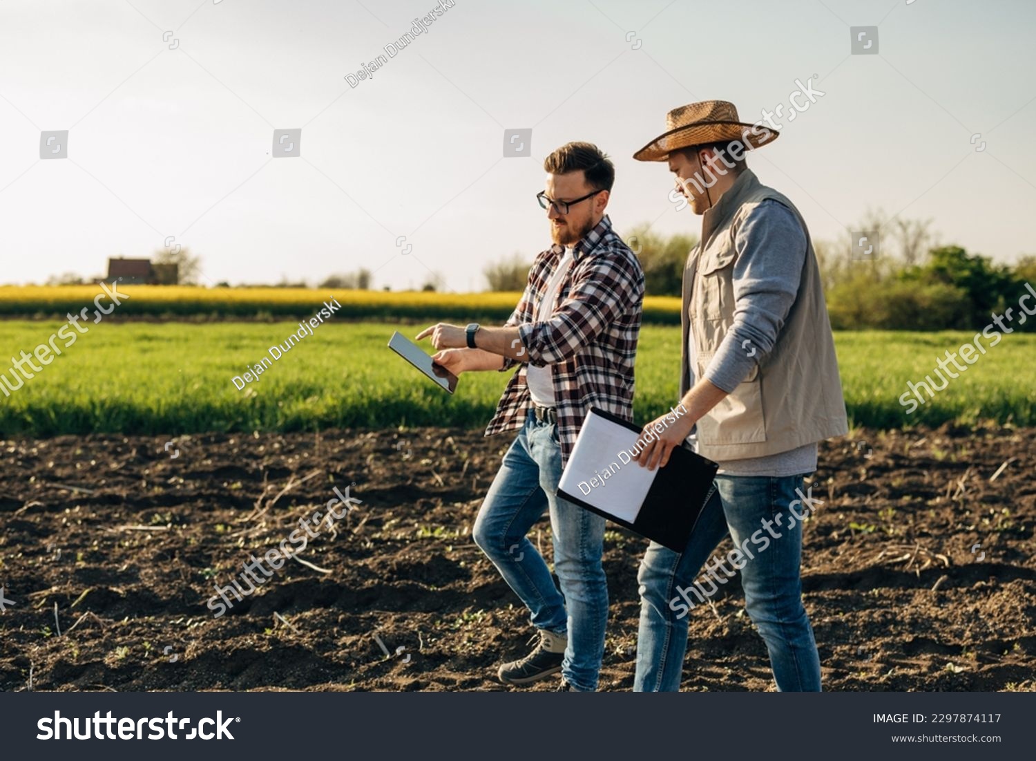 Inspector and a farmer walk across the farmland. The inspector points to a tablet he is holding. #2297874117