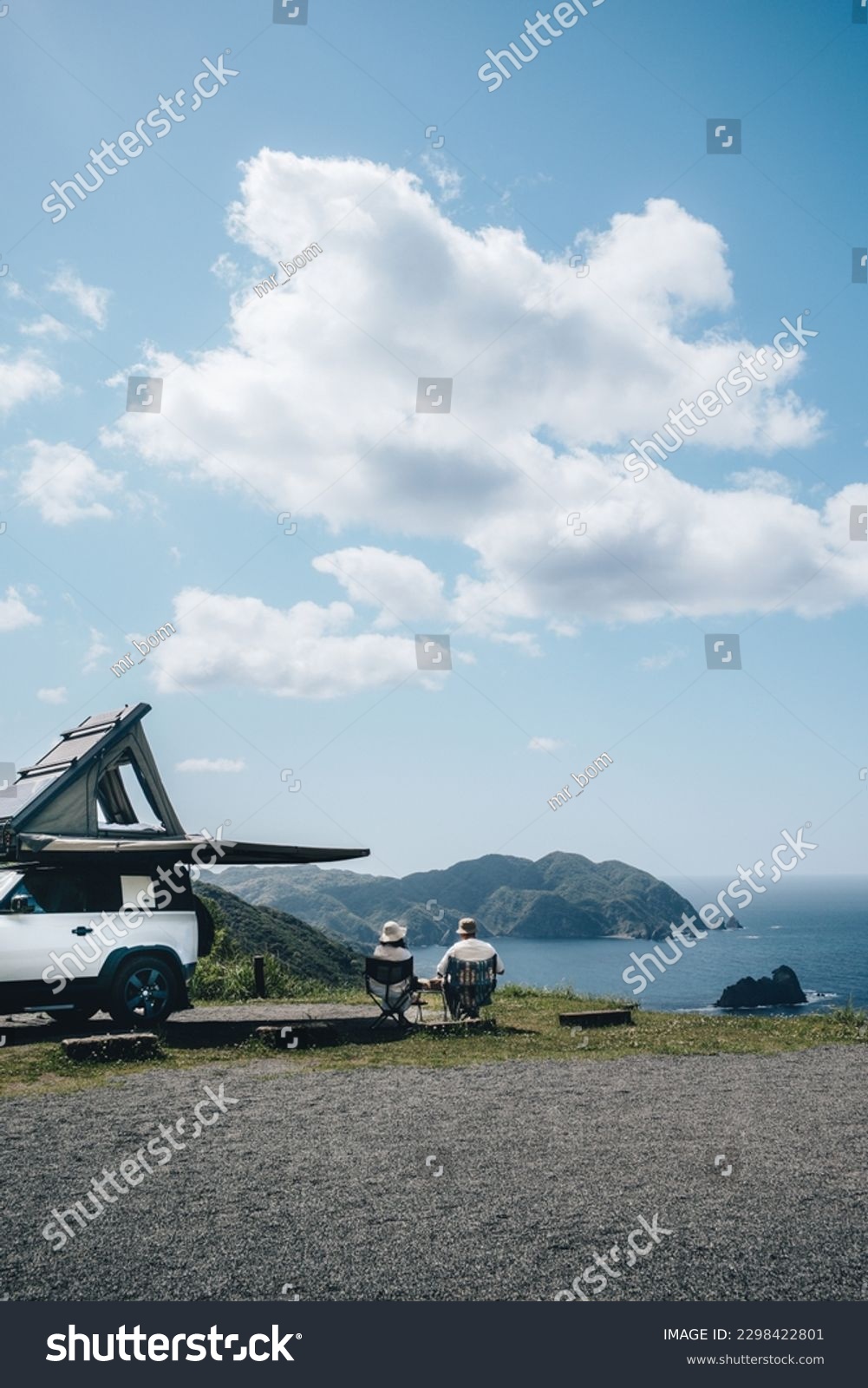 Couple sitting in a camping chair in nature with a view of Island in a beautiful blue sky with an overlanding car with a rooftop tent and an awning. #2298422801