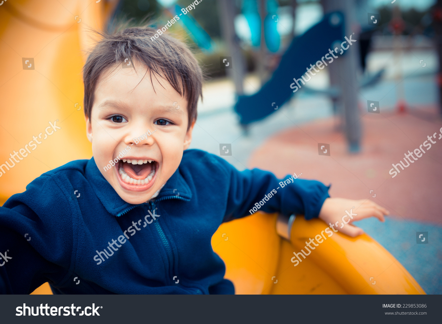 Cute Asian Caucasian mixed race toddler happily playing on a slide in a playground outside in the summer sun #229853086