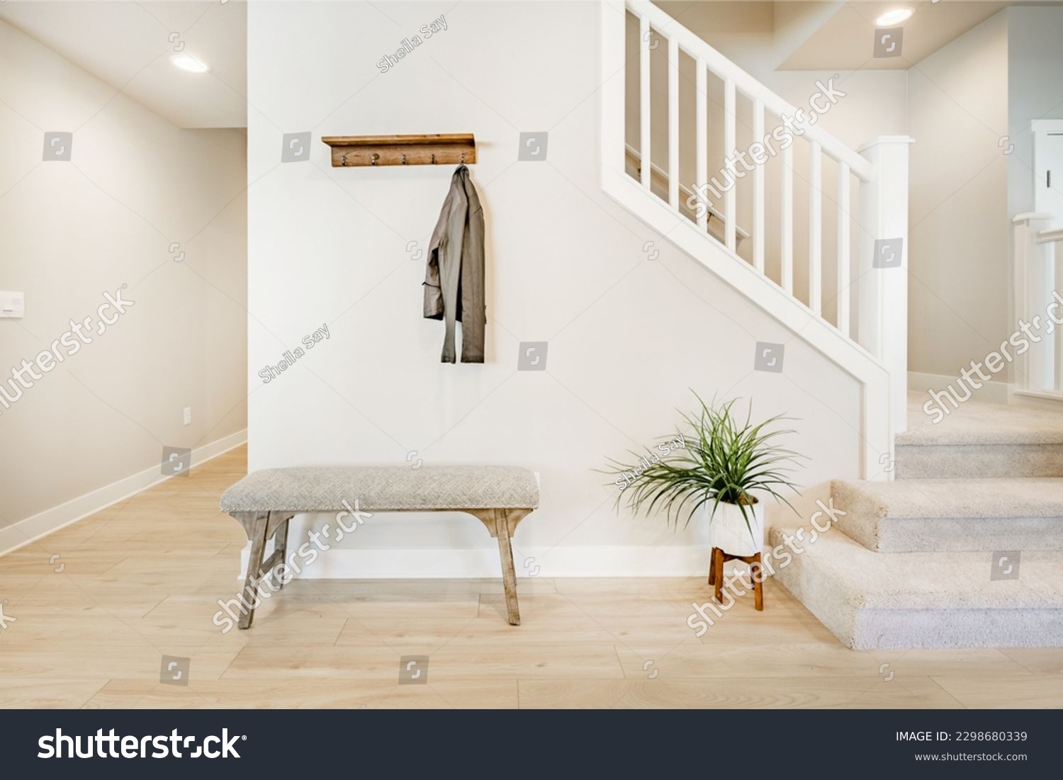 Bright and airy entry foyer with white wall stair case light colored hard wood flooring dark walnut front door entry coat rack hooks to a welcoming interior #2298680339