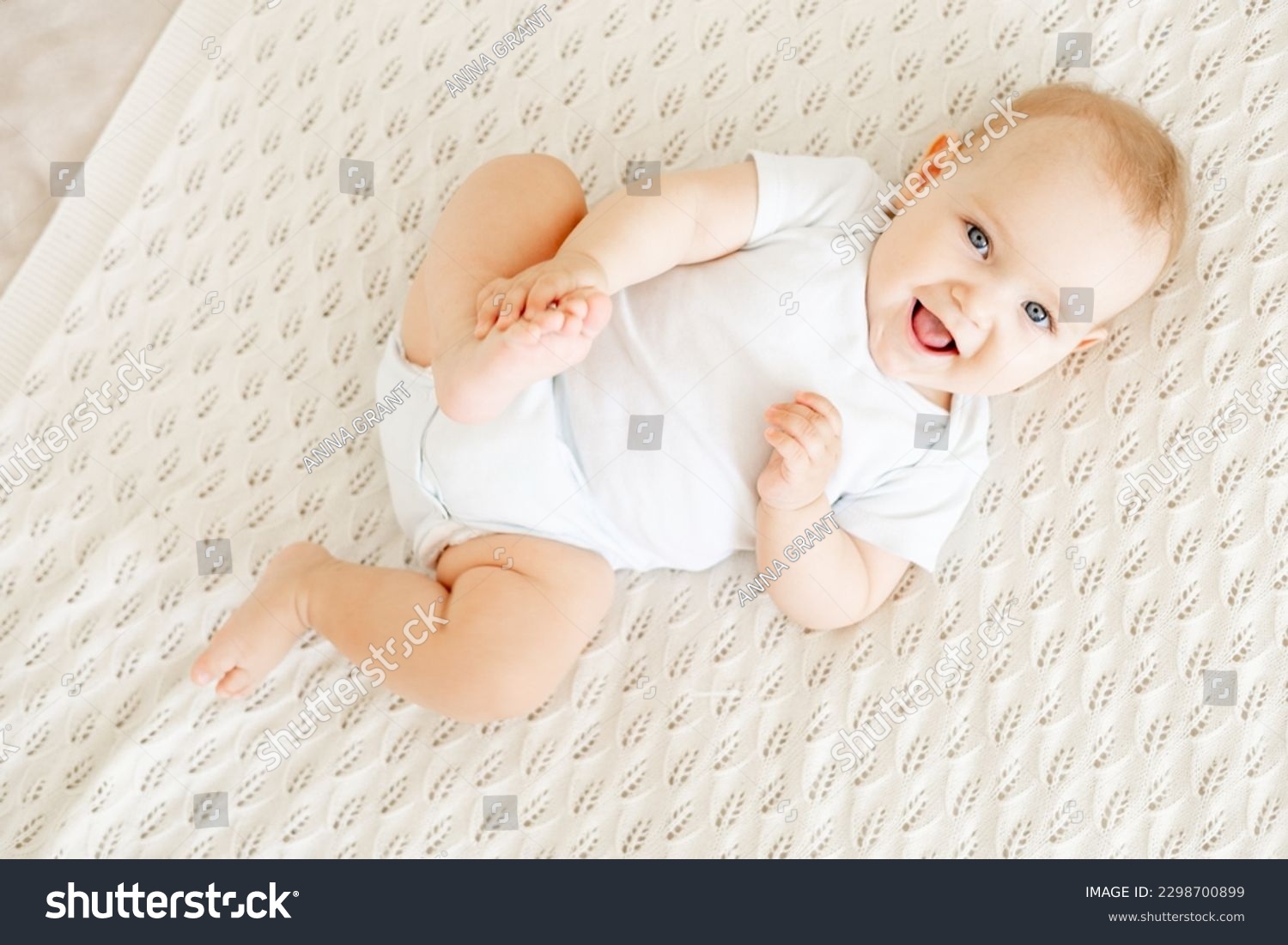 close-up of a laughing happy baby on a white cotton bed in a bright bedroom, a small smiling baby boy or girl lying on her back #2298700899