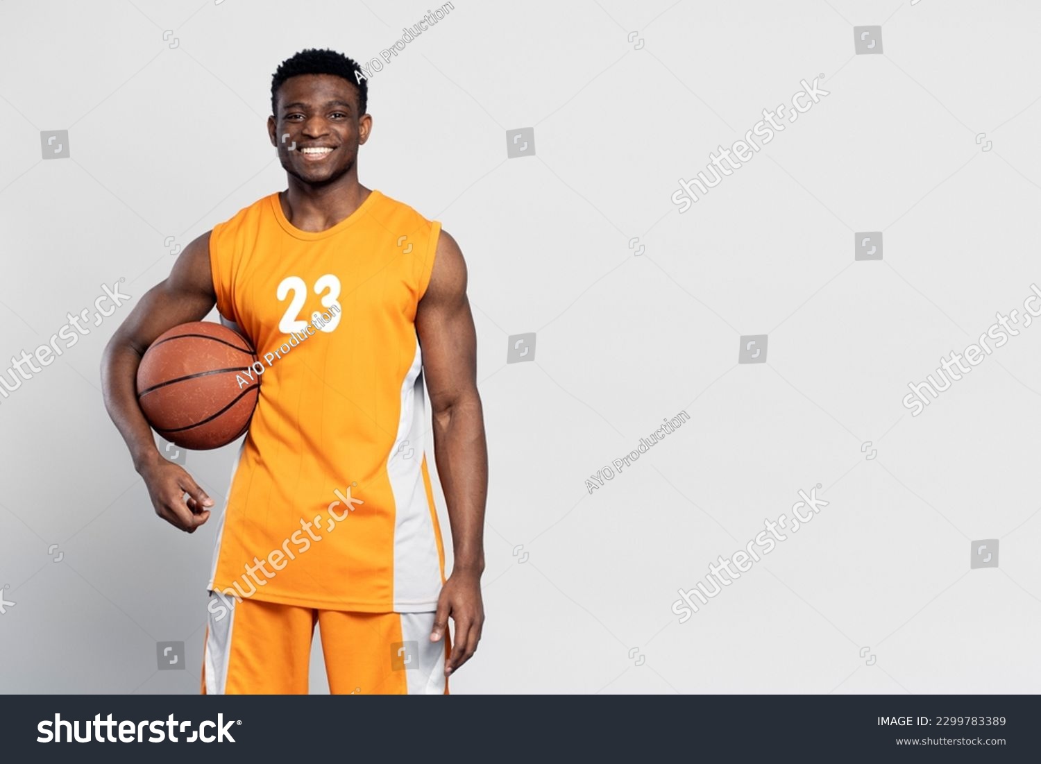 Portrait of confident smiling African American man, professional basketball player holding ball isolated on white background. Sportsman wearing orange basketball uniform looking at camera, copy space #2299783389