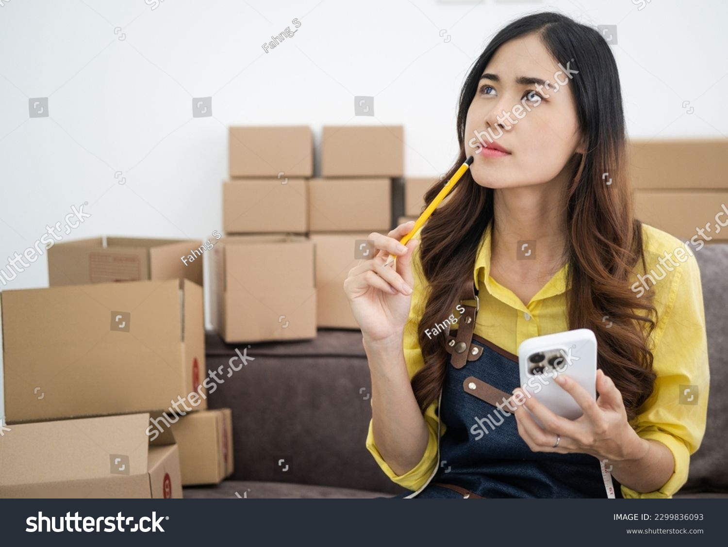 Young asian online seller businesswoman working shipping at home looking at mobile phone for online orders and thinking about her business future, good for online seller business concept. #2299836093