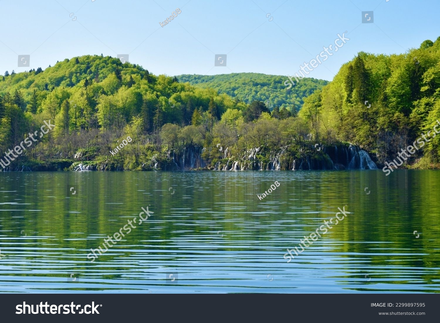 Waterfalls flowing into Kozjak lake at Plitvice lakes in Lika-Senj county, Croatia with forest covered hills above #2299897595