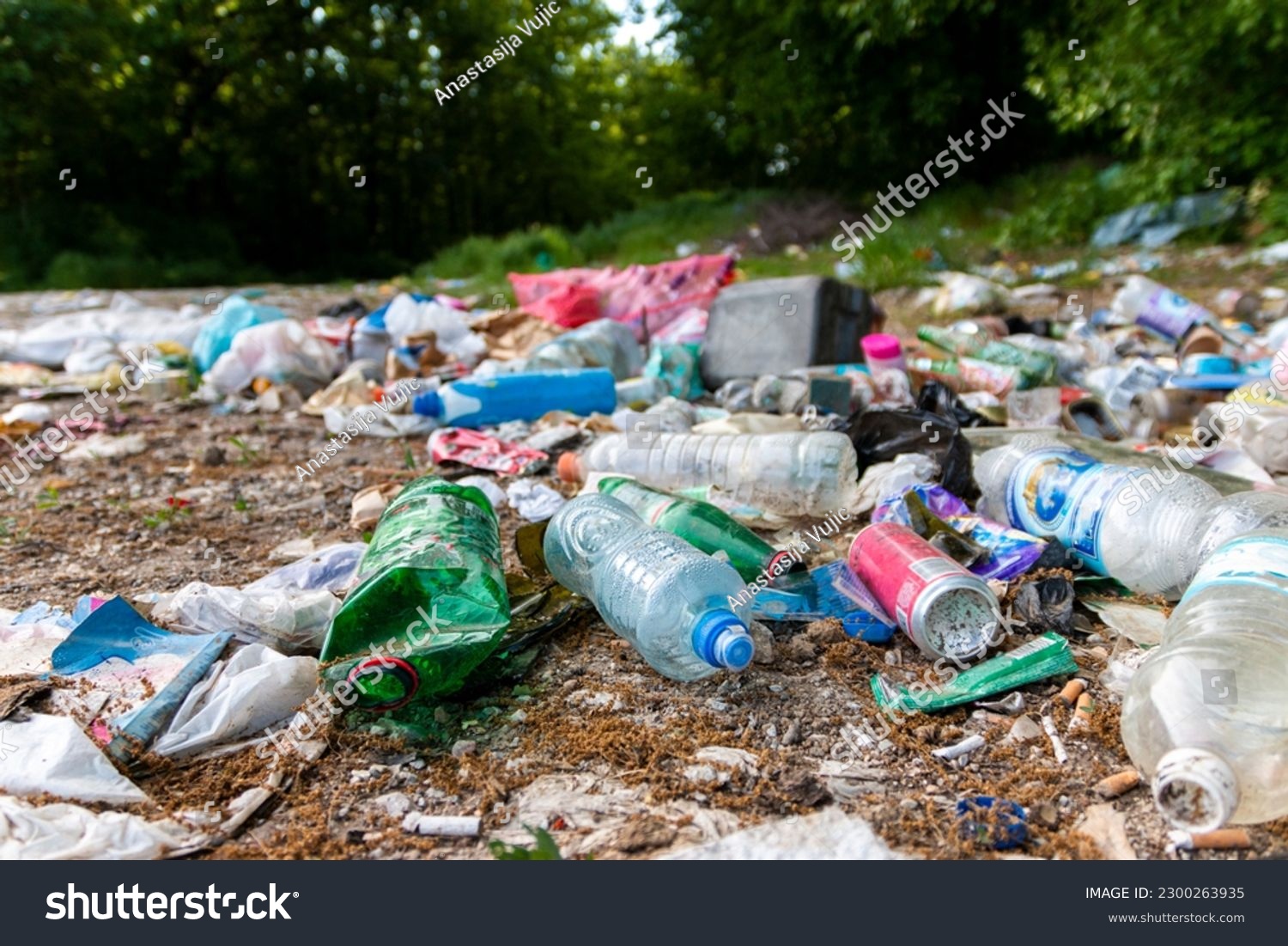 Piles of garbage in the forest, random dumping in nature. Stink heap, plastic bag and bottles, rubbish in polluted green  grass of nature landscape background. The concept of human pollution of forest #2300263935