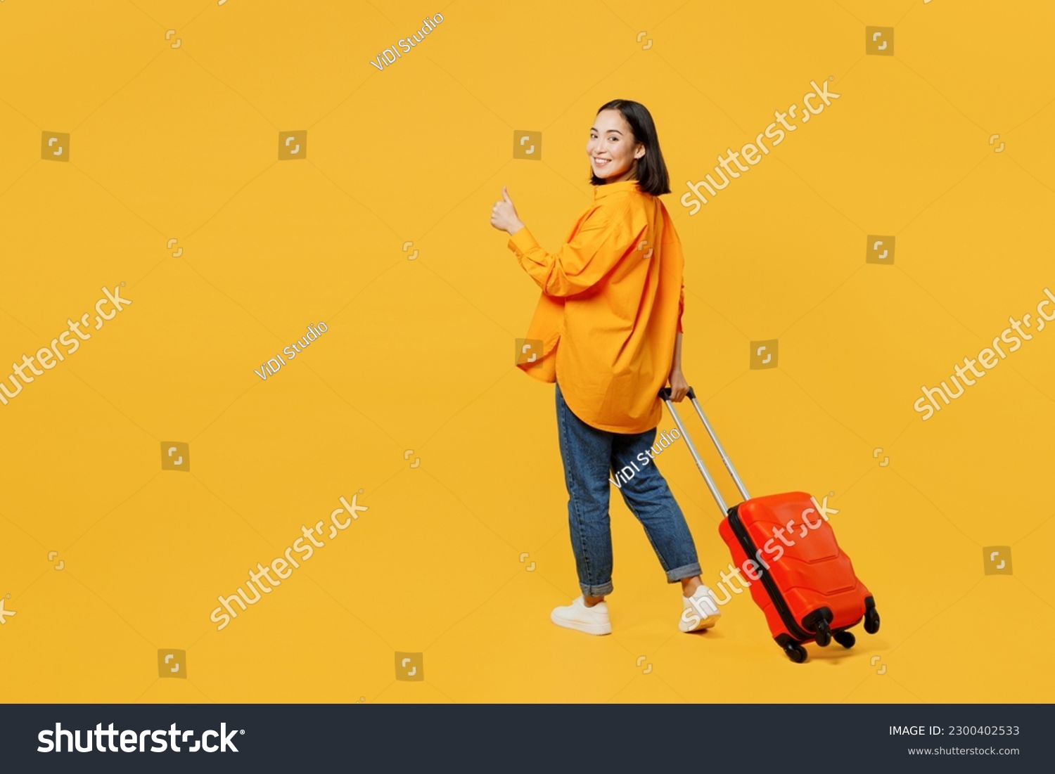 Back view young woman wear summer clothes walk go with suitcase bag show thumb up isolated on plain yellow background. Tourist travel abroad in free time rest getaway. Air flight trip journey concept #2300402533