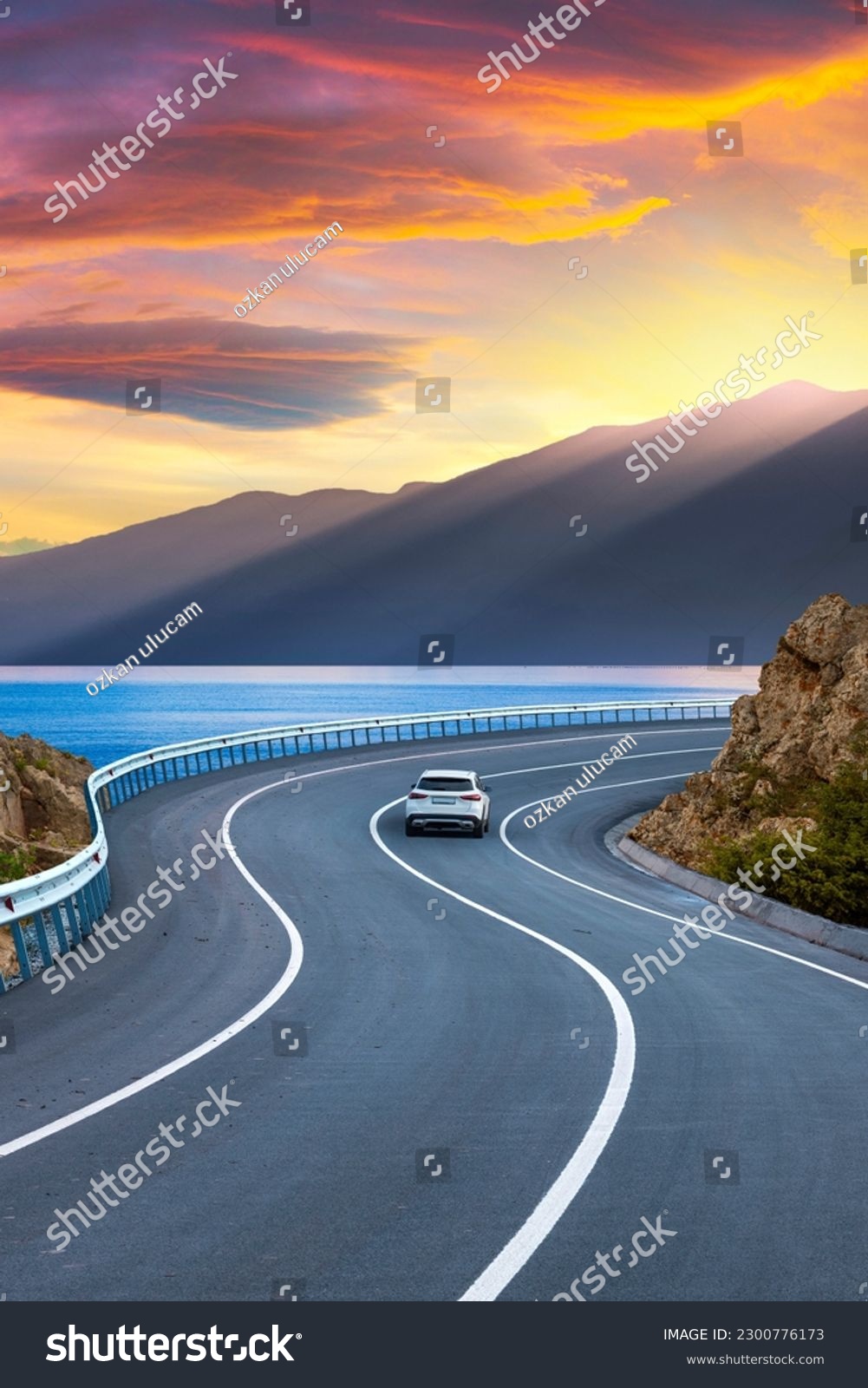 Car in motion in the highway landscape under the coastal road. Road landscape at colorful sunset. Car driving on the highway. Nature scenery on sea beach. Travel journey for summer trip on road. #2300776173