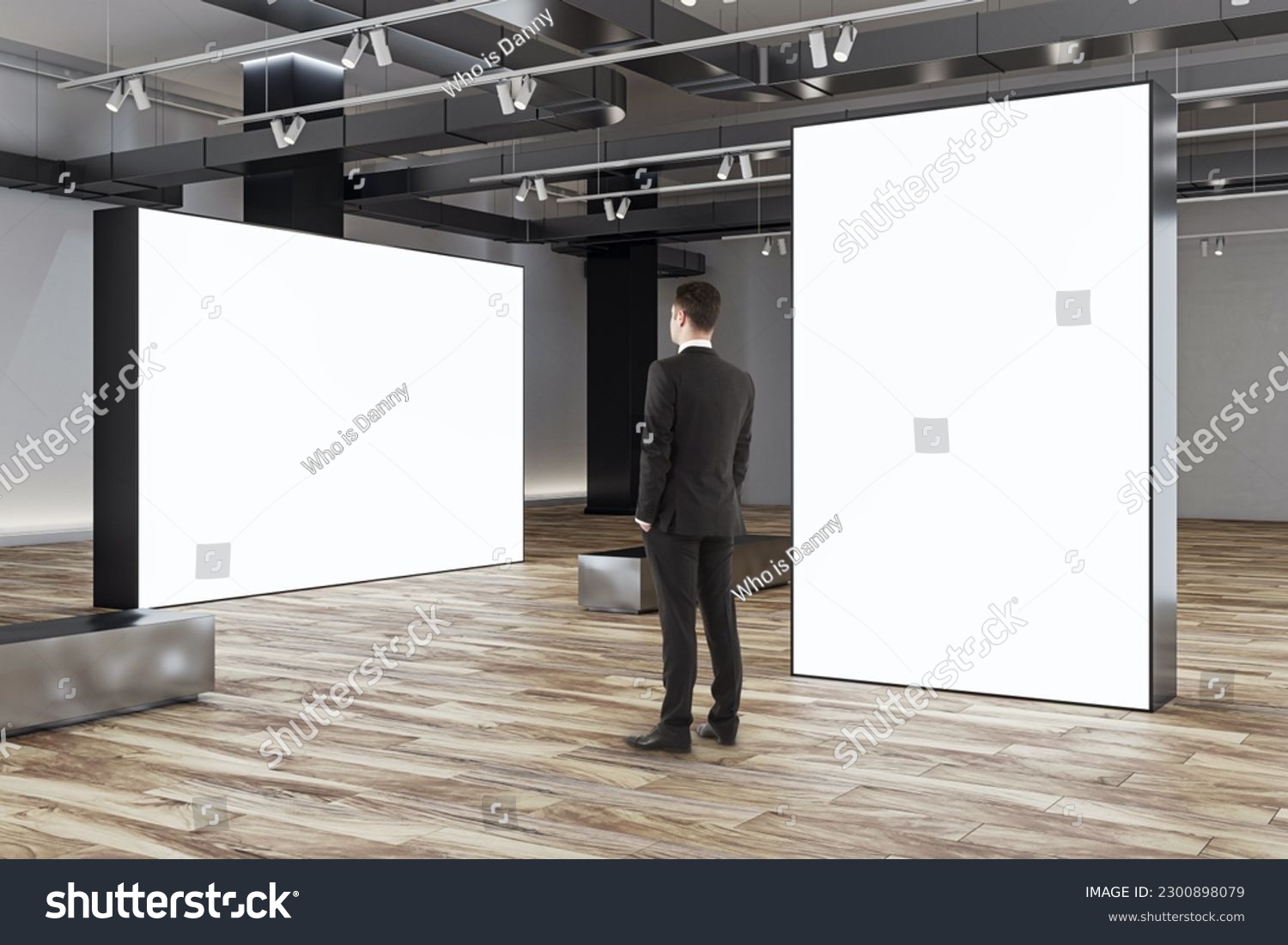 Businessman looks at blank white partitions with place for advertising poster or marketing campaign in stylish gallery hall with metallic benches on wooden floor and grey wall background, mockup #2300898079
