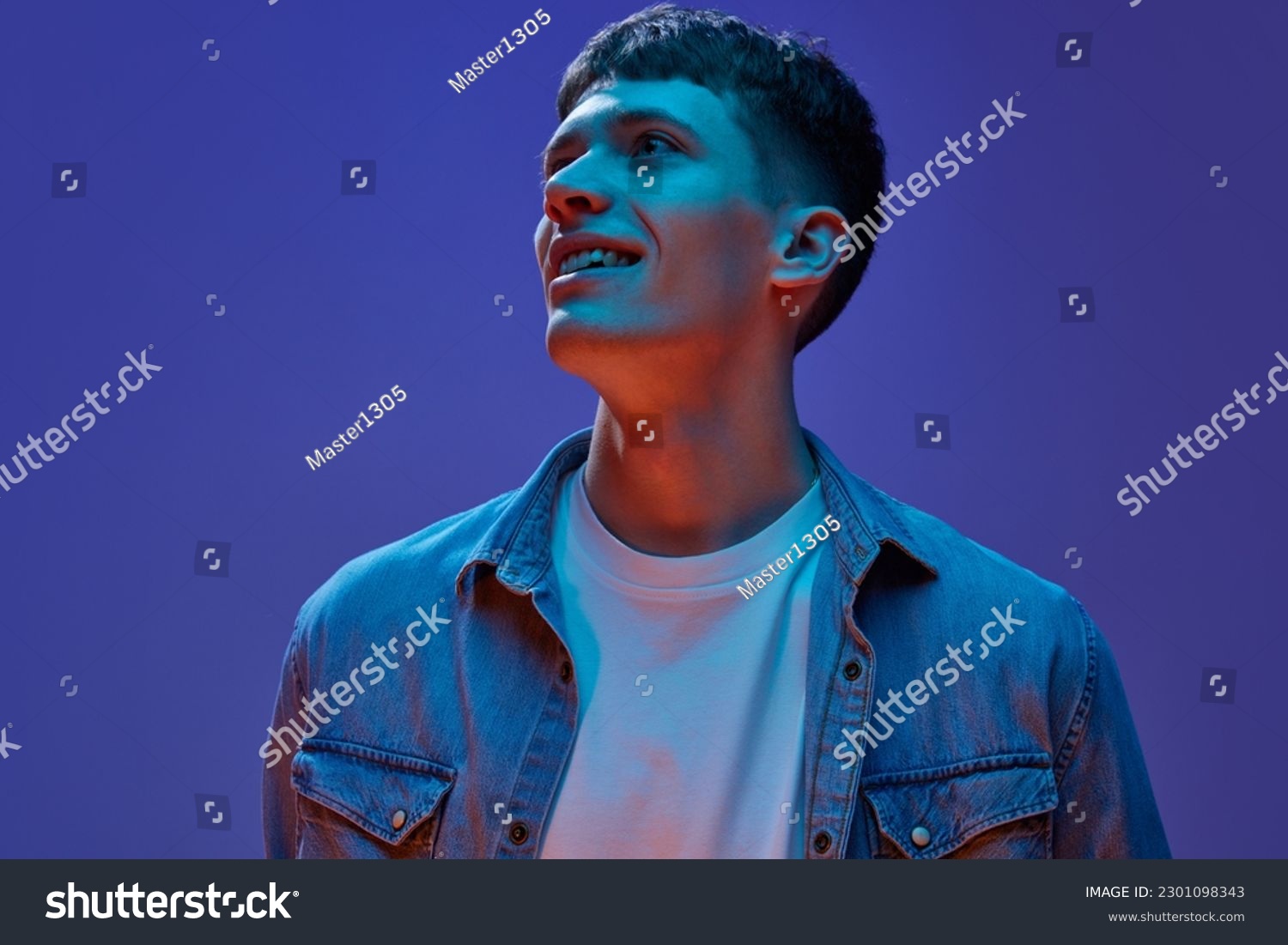 Portrait of young handsome guy in jeans shirt and white t-shirt design with smile, looking away against gradient purple background in neon light. Concept of human emotions, lifestyle, youth #2301098343