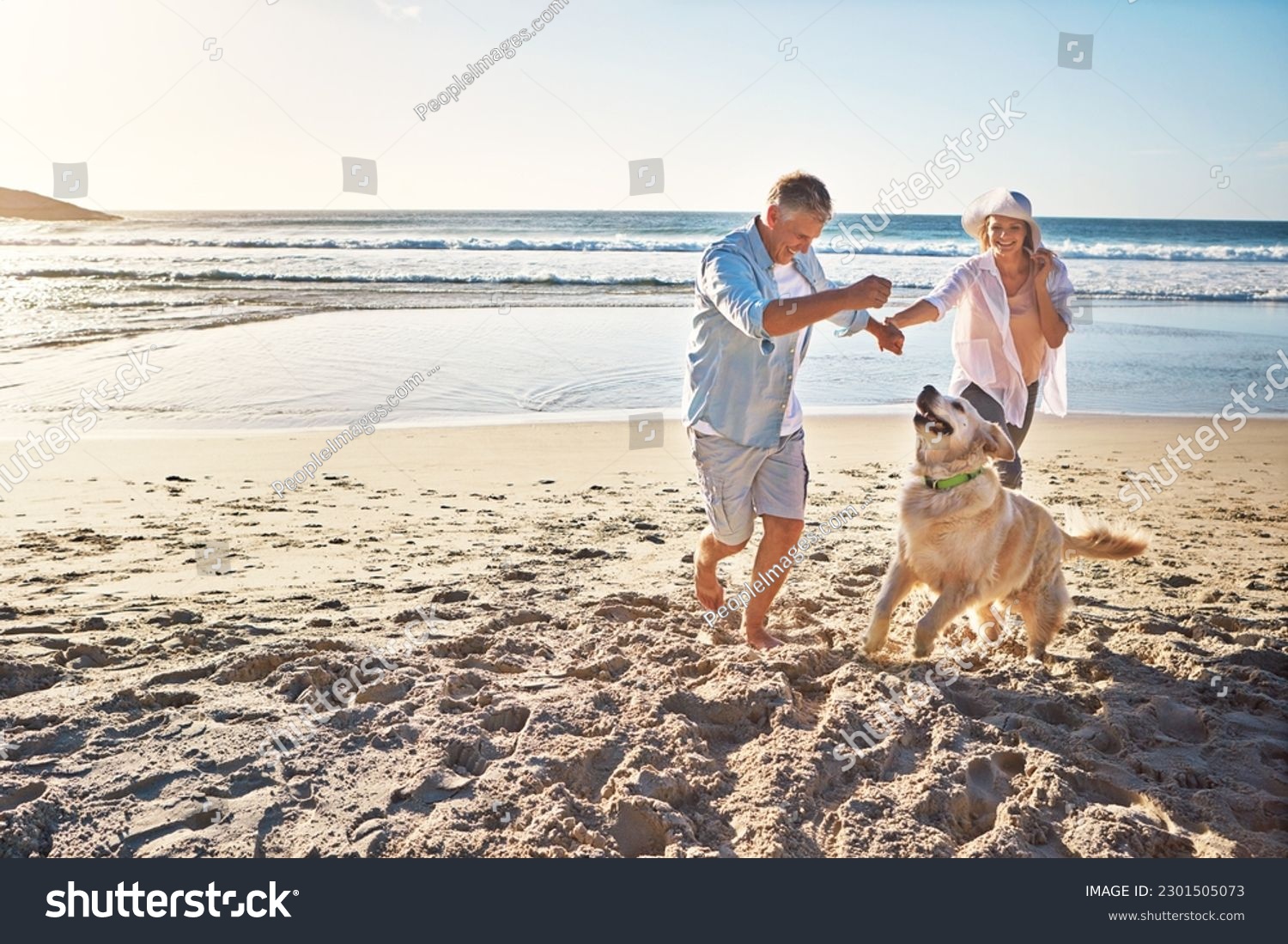 Happy couple, holding hands and at the beach with a dog in summer for retirement travel in Indonesia. Smile, playful and an elderly man and woman on a walk at the sea with a pet for play and holiday #2301505073