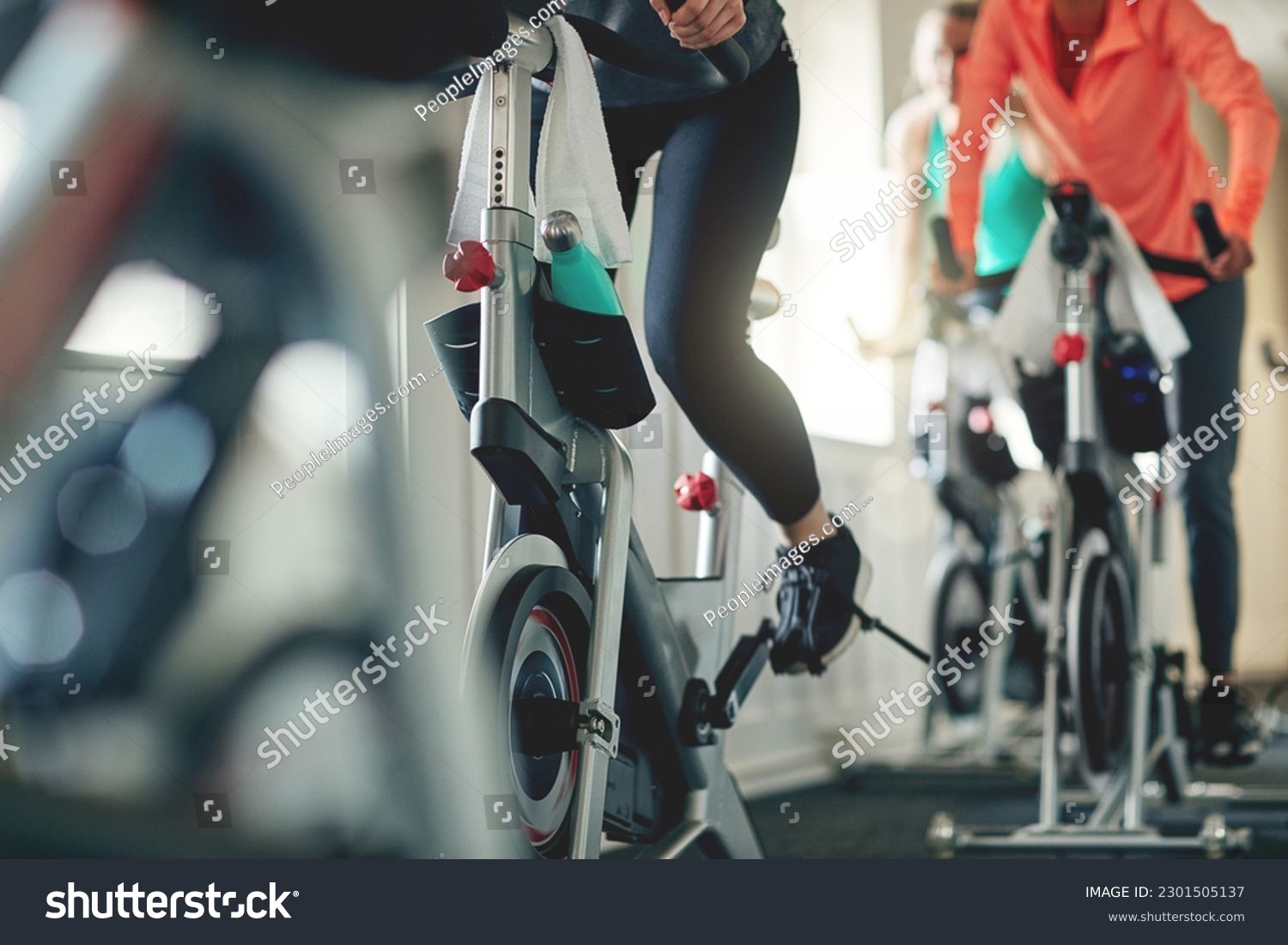 Fitness, legs and exercise bike with people in a gym for a cardio or endurance spinning class workout. Health, wellness and energy with a sporty athlete group training or cycling in a sports center #2301505137