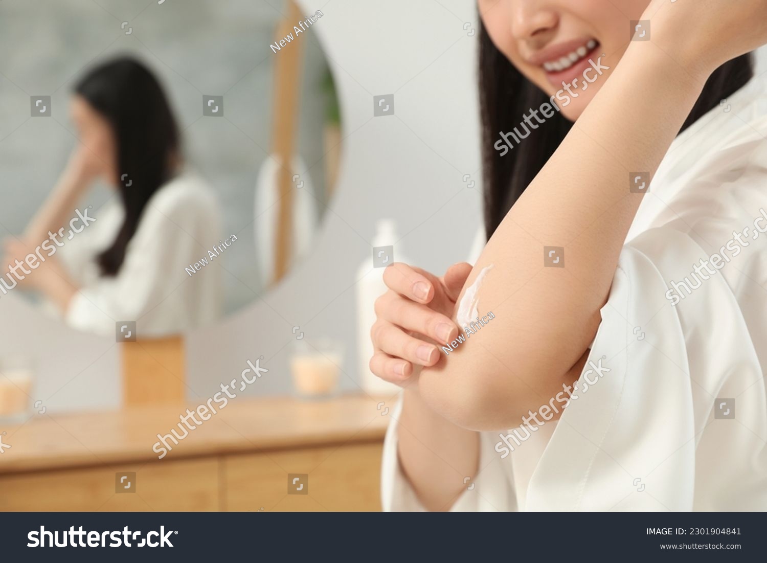 Young woman applying body cream on elbow in bathroom, closeup. Space for text #2301904841