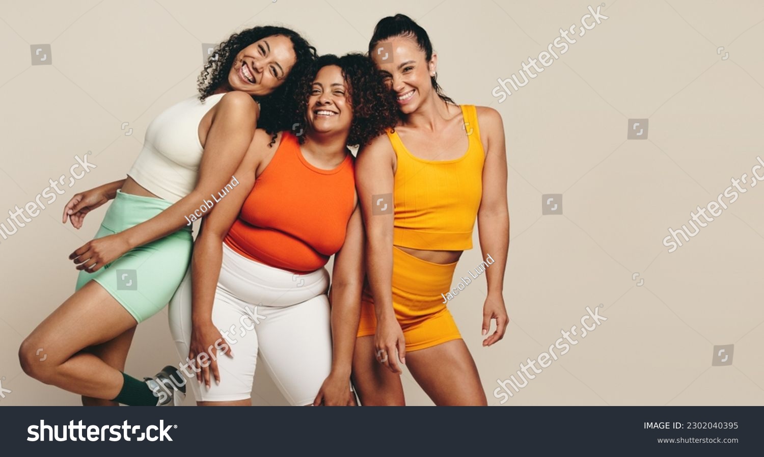 Female athletes smiling at the camera as they stand together in a studio, wearing fitness clothing. Group of young sports women expressing their love for sport, exercise and a health lifestyle. #2302040395