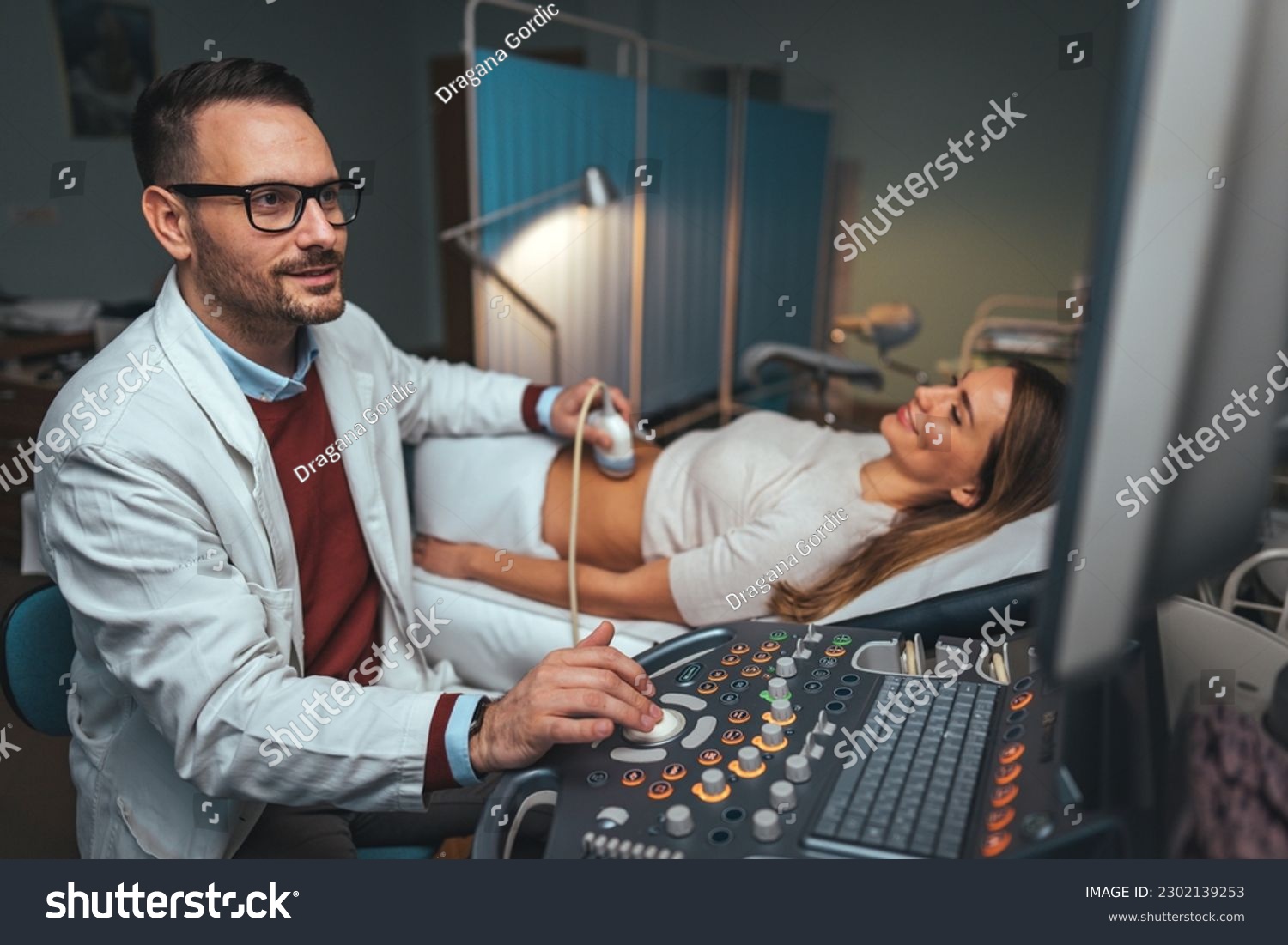 Selective focus on ultrasound scanner device in the hand of a professional doctor examining his patient doing abdominal ultrasound scanning sonogram sonography sonographer early pregnancy #2302139253