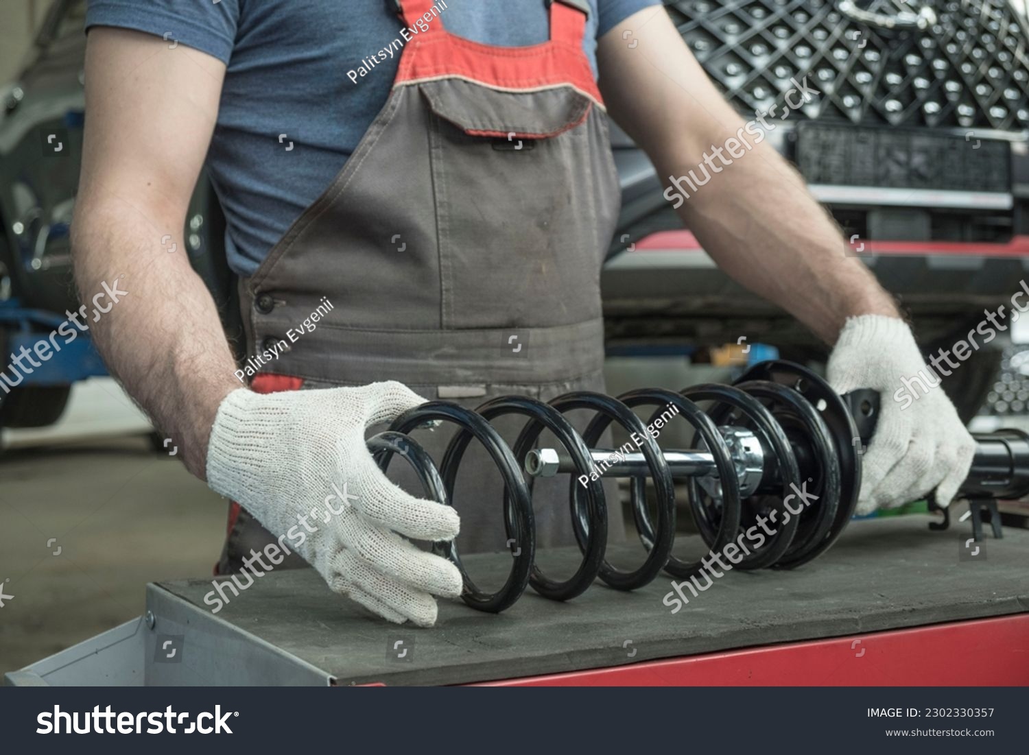 An auto mechanic holds a new shock absorber strut and a spring in his hands. The specialist evaluates the compatibility of the car suspension parts. Car maintenance. #2302330357