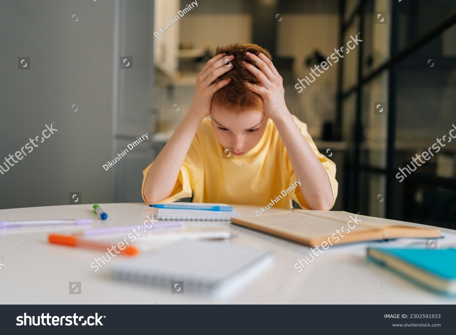 Portrait of exhausted pupil boy tired from studying holding head head with hands sitting at desk with paper copybook, looking down. Frustrated child schoolboy doing homework at home. #2302591933