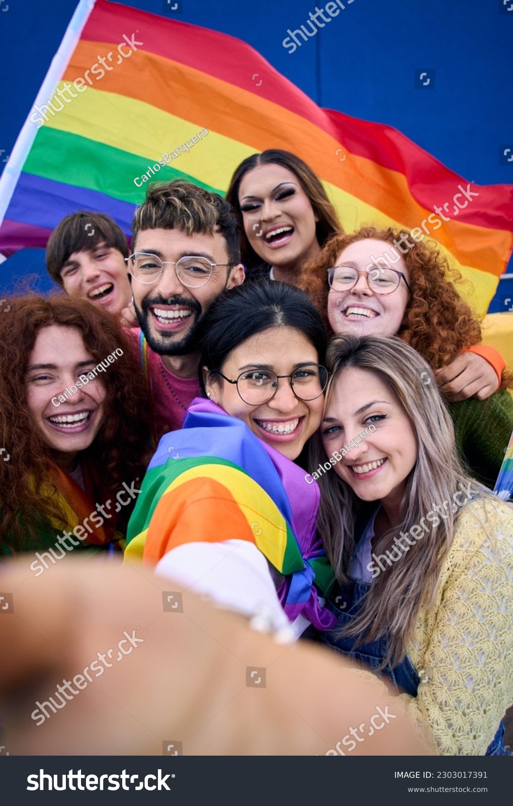 Vertical selfie of LGBT group of young people celebrating gay pride day holding rainbow flag together. Homosexual community smiling taking cheerful self portrait. Lesbian couple friends generation z. #2303017391