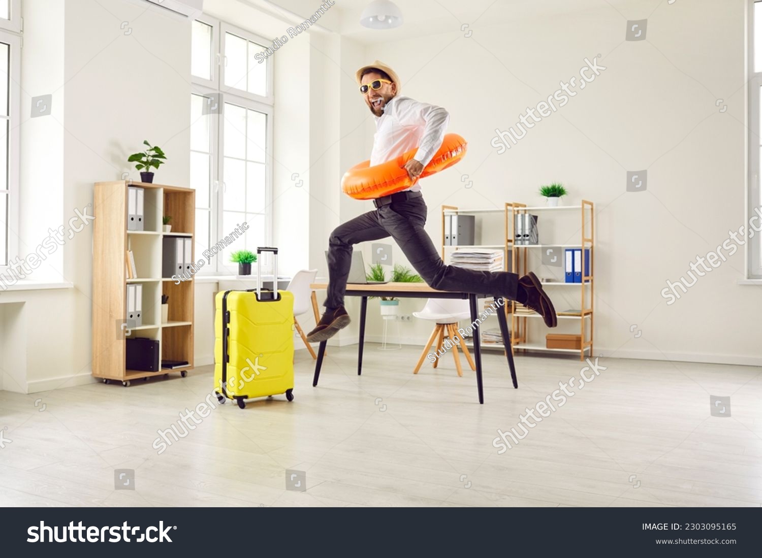 Happy, funny, energetic, excited man office worker in a sun hat, sunglasses and beach ring jumping and having fun in the office. Summer holiday, vacation, work leave, annual leave concept #2303095165