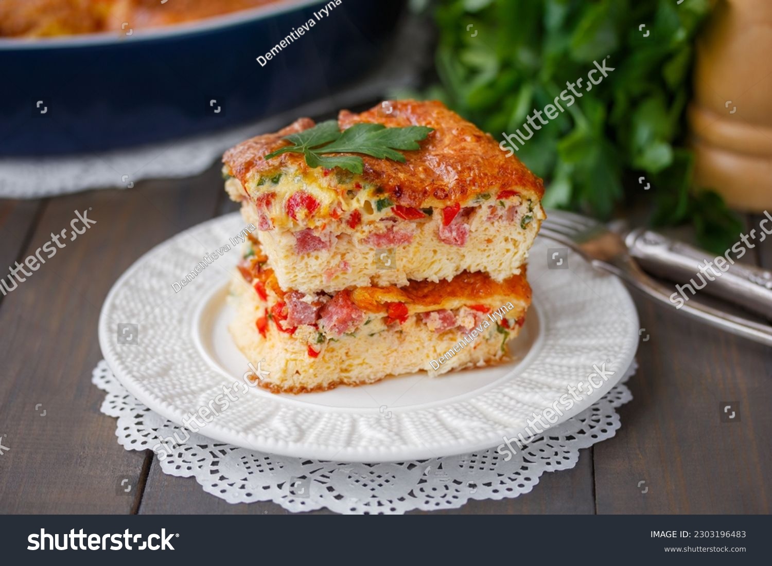 Fluffy Oven Baked omelette with cheese, tomato and ham sliced on a white ceramic plate. Vegetable Soufflé or Puffy omelet. Selective focus, horizontal, closeup, wooden table. #2303196483