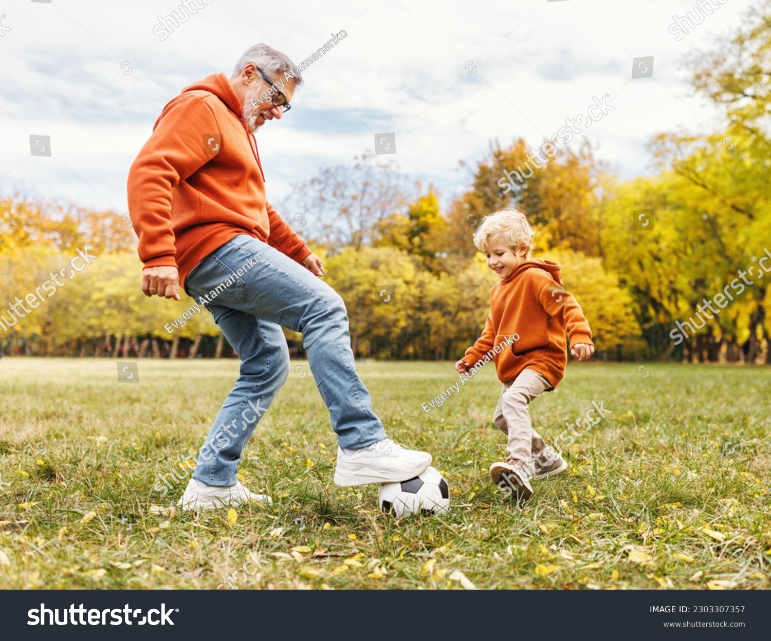 Happy family grandfather and grandson play football on lawn in the park
 #2303307357