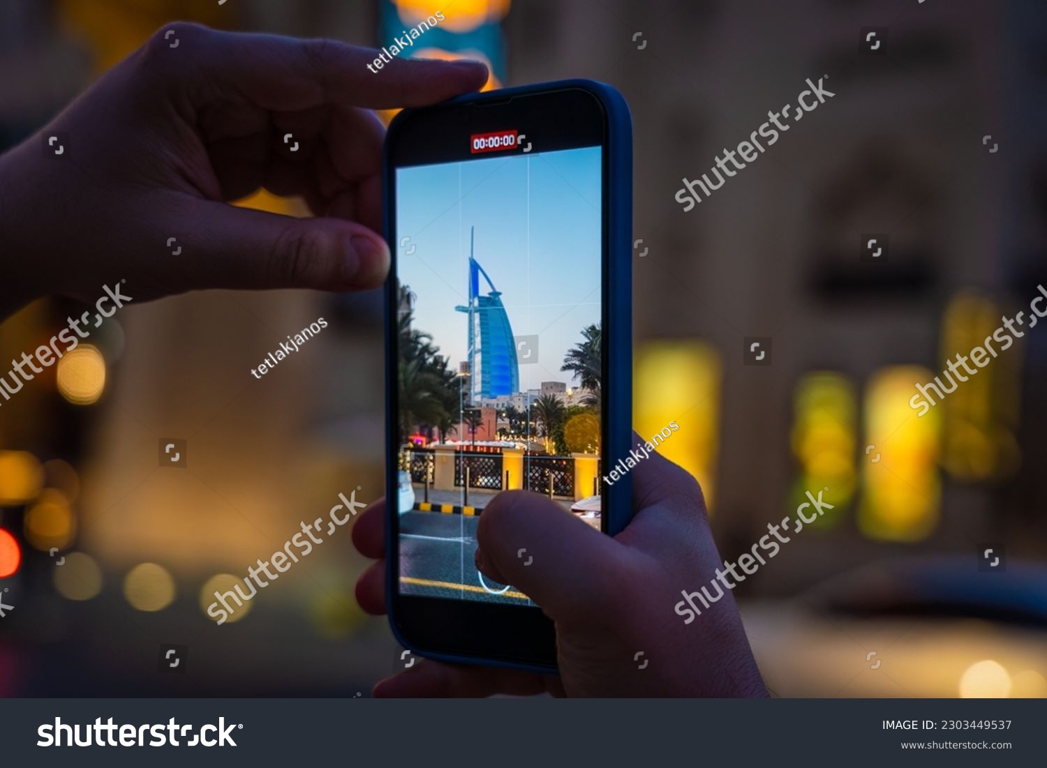 A young woman takes a mobile phone video of Dubai's Burj Al Arab hotel during the blue hour after sunset. #2303449537