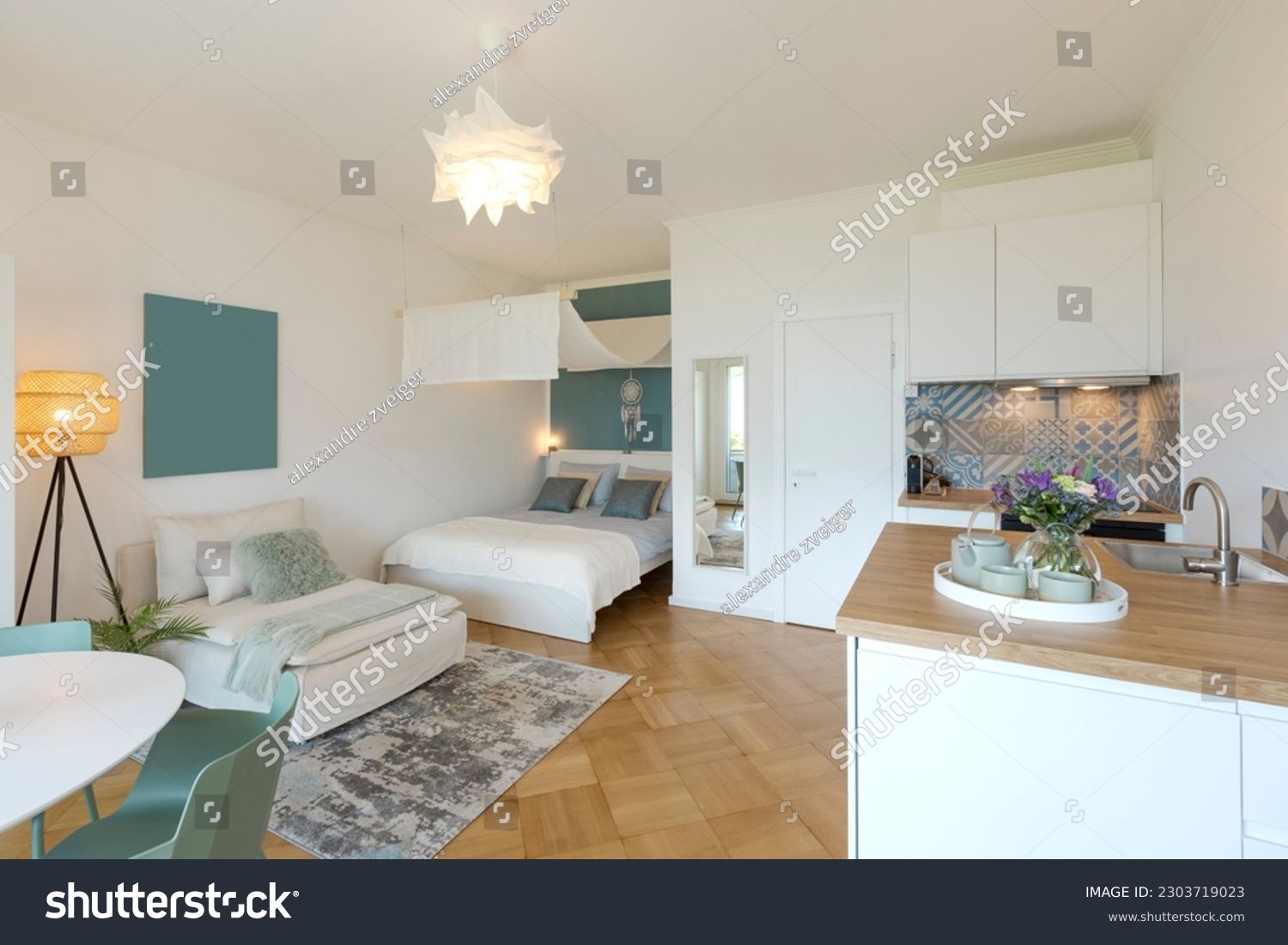 General view of a stylish modern studio apartment. There is a small kitchen with a wooden counter, a double bed and a single bed, and a table with chairs. No one inside #2303719023