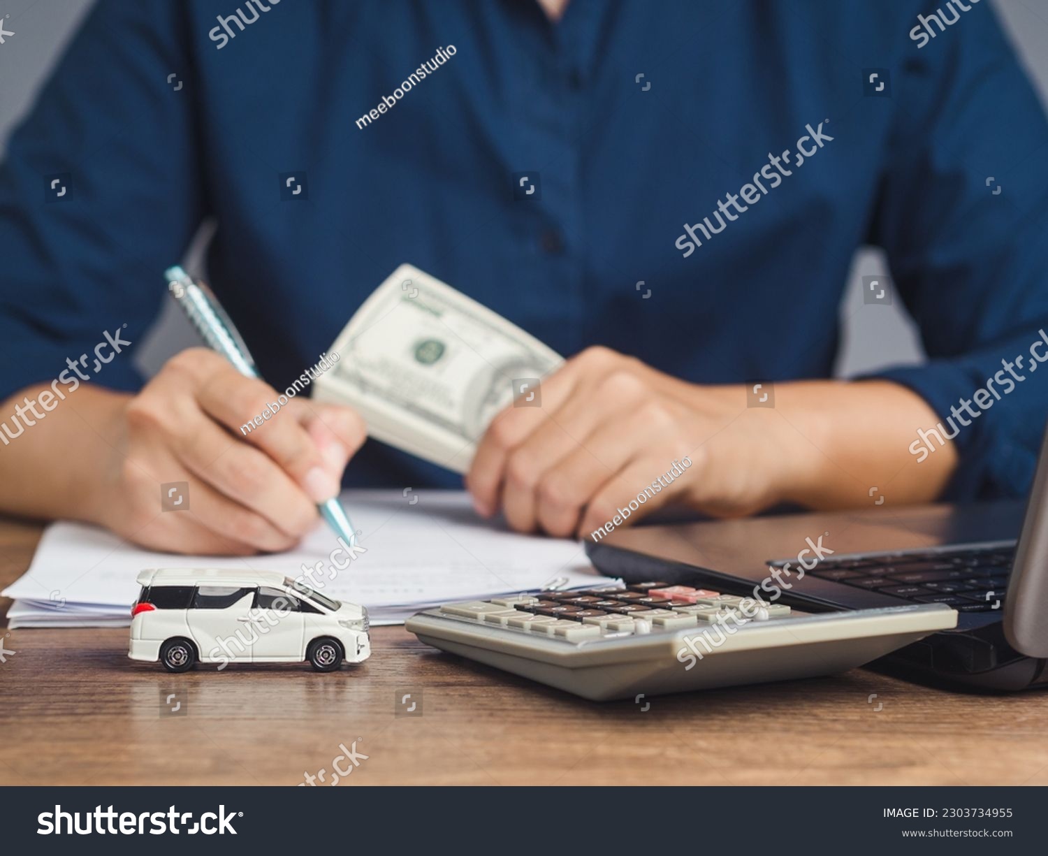 Car loan or Title loan. US dollar bills in a hand businessman while sitting at the table. Miniature a red car model, a calculator, and a laptop on a table. Car finance and insurance concept #2303734955