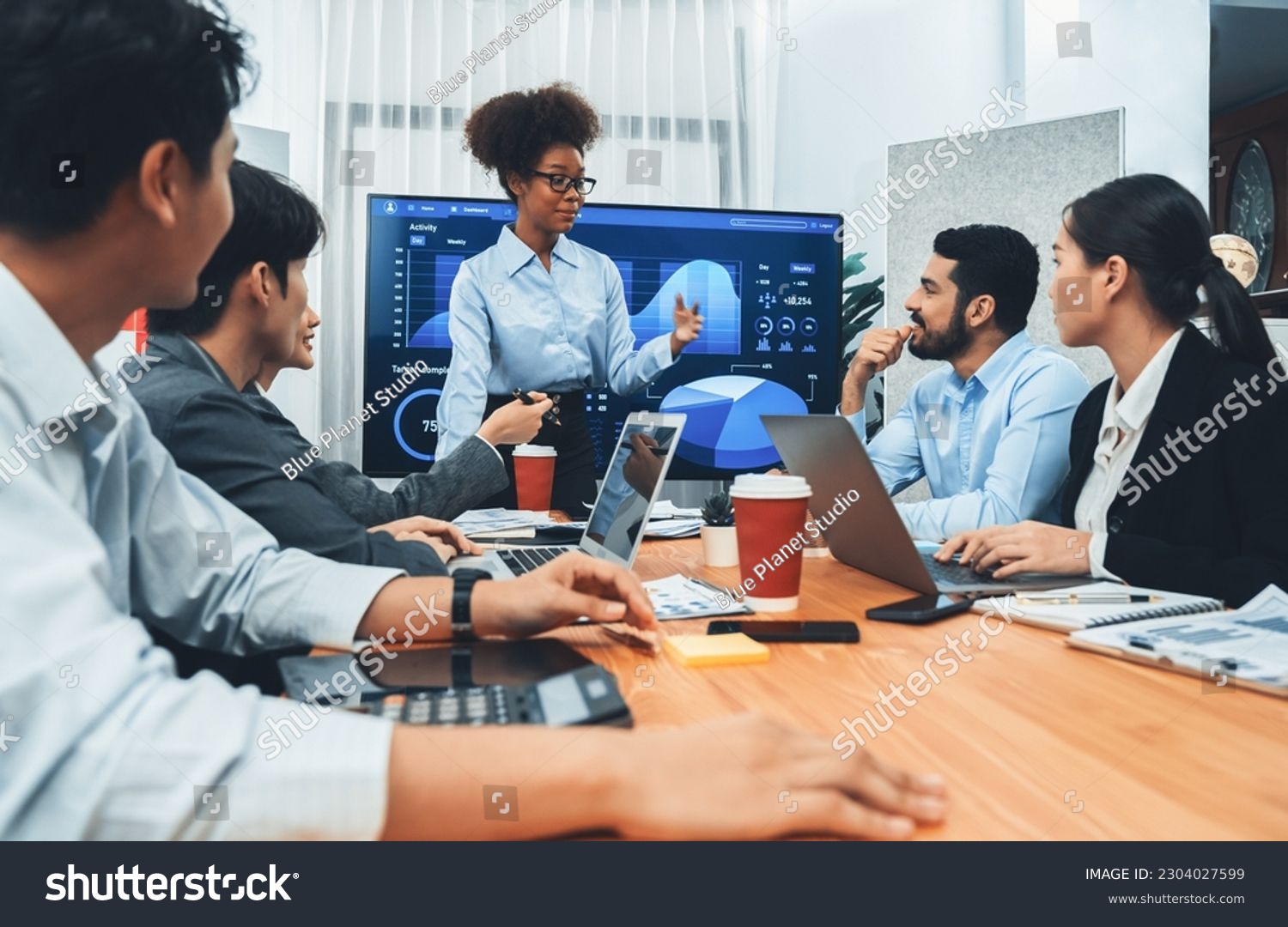 Young african businesswoman presenting data analysis dashboard on TV screen in modern meeting. Business presentation with group of business people in conference room. Concord #2304027599