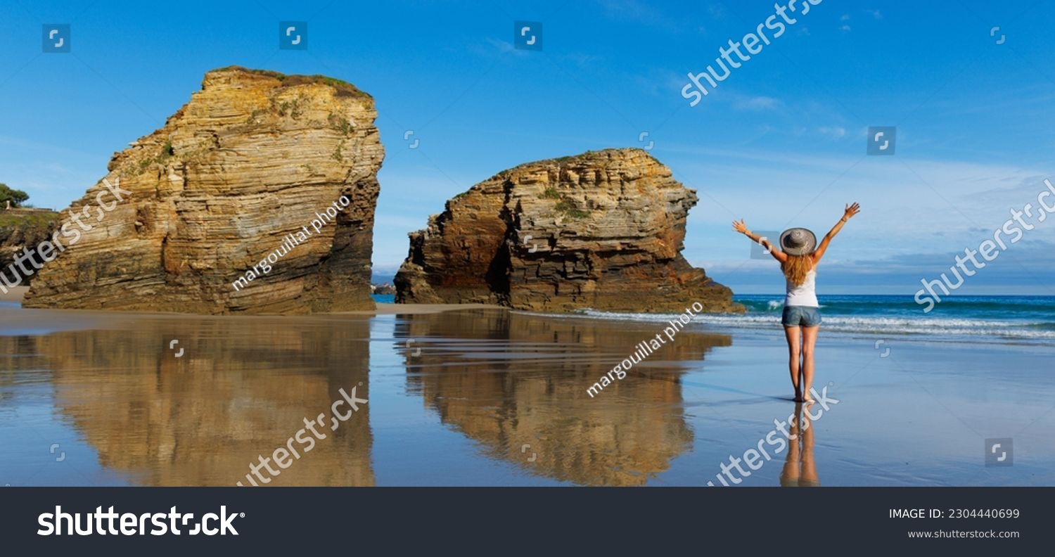 Woman with arms raised enjoying atlantic ocean and rock formation- cathedral beach with arch and cave- Galicia,  Spain #2304440699
