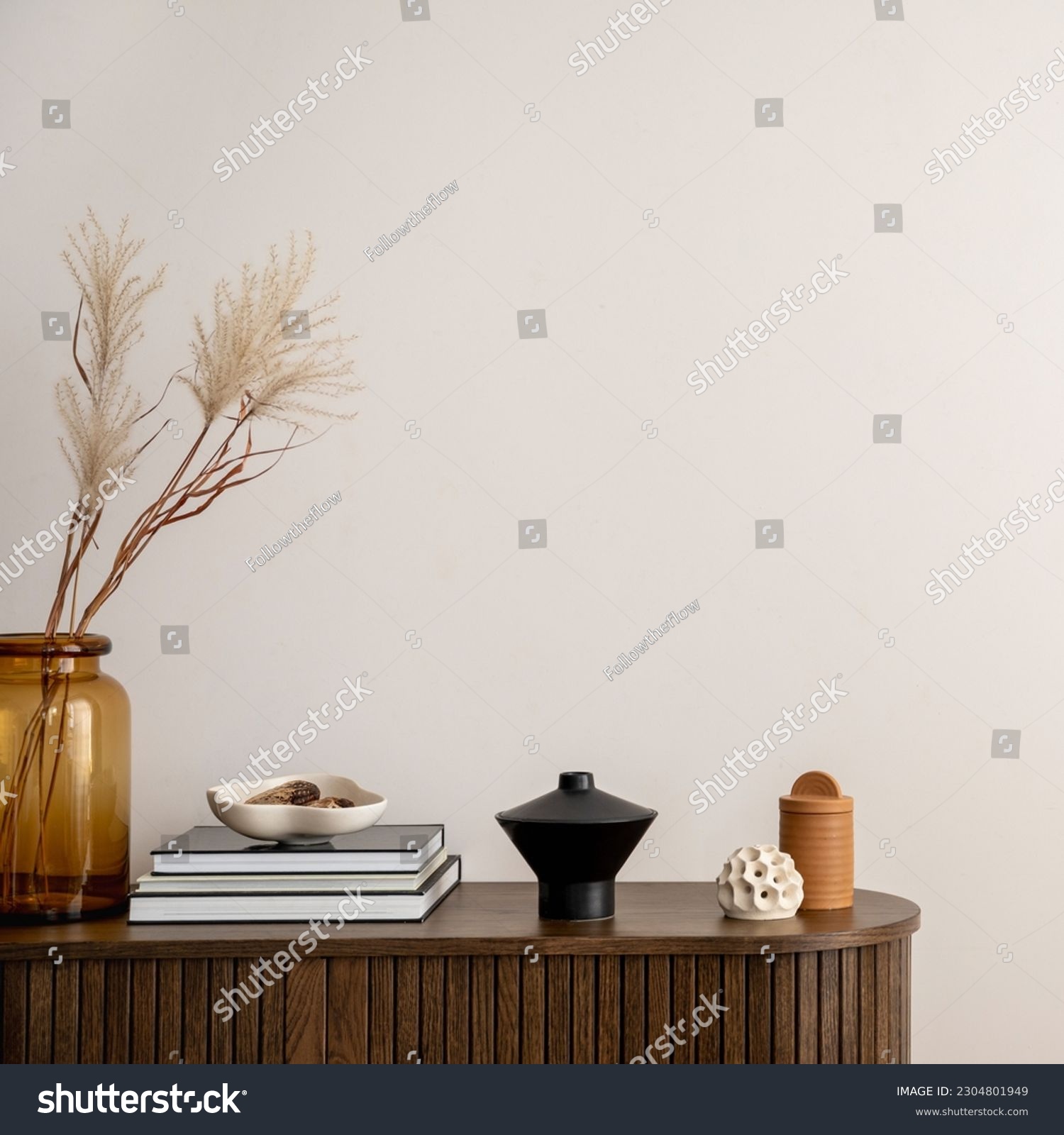 Minimalist composition of living room interior with copy space, wooden commode, vase with dried flowers, candle, black books and personal accessories. Home decor. Template.  #2304801949
