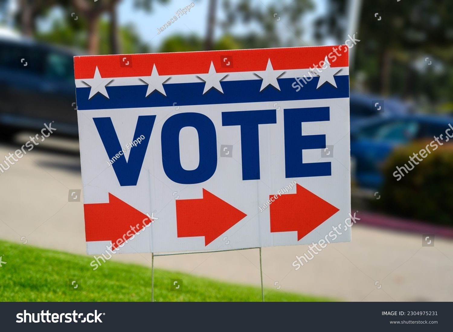 A VOTE sign at a polling place on green grass near a parking lot #2304975231