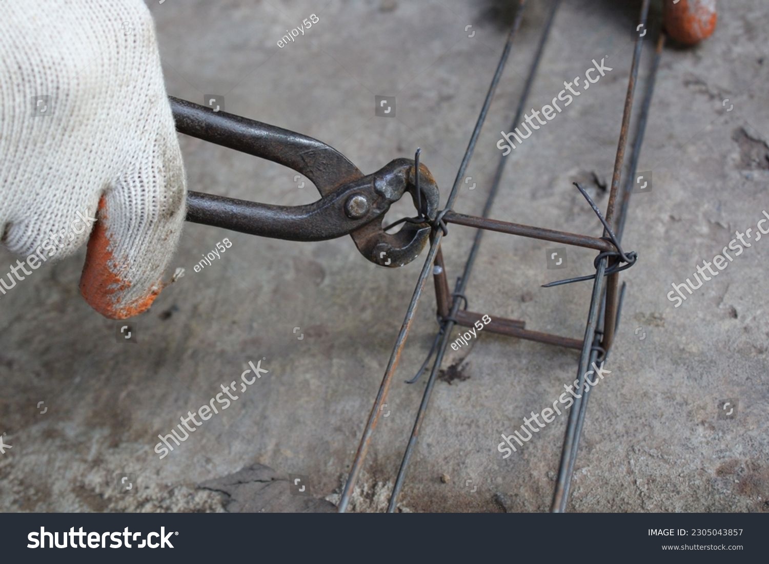 Workers hands using steel wire and pincers to secure rebar before concrete is poured over it #2305043857