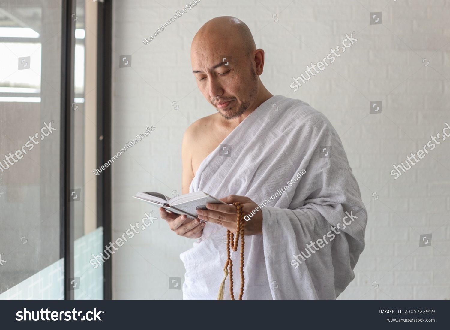 Muslim man wearing traditional white ihram clothes, reading quran while holds prayer beads.  #2305722959