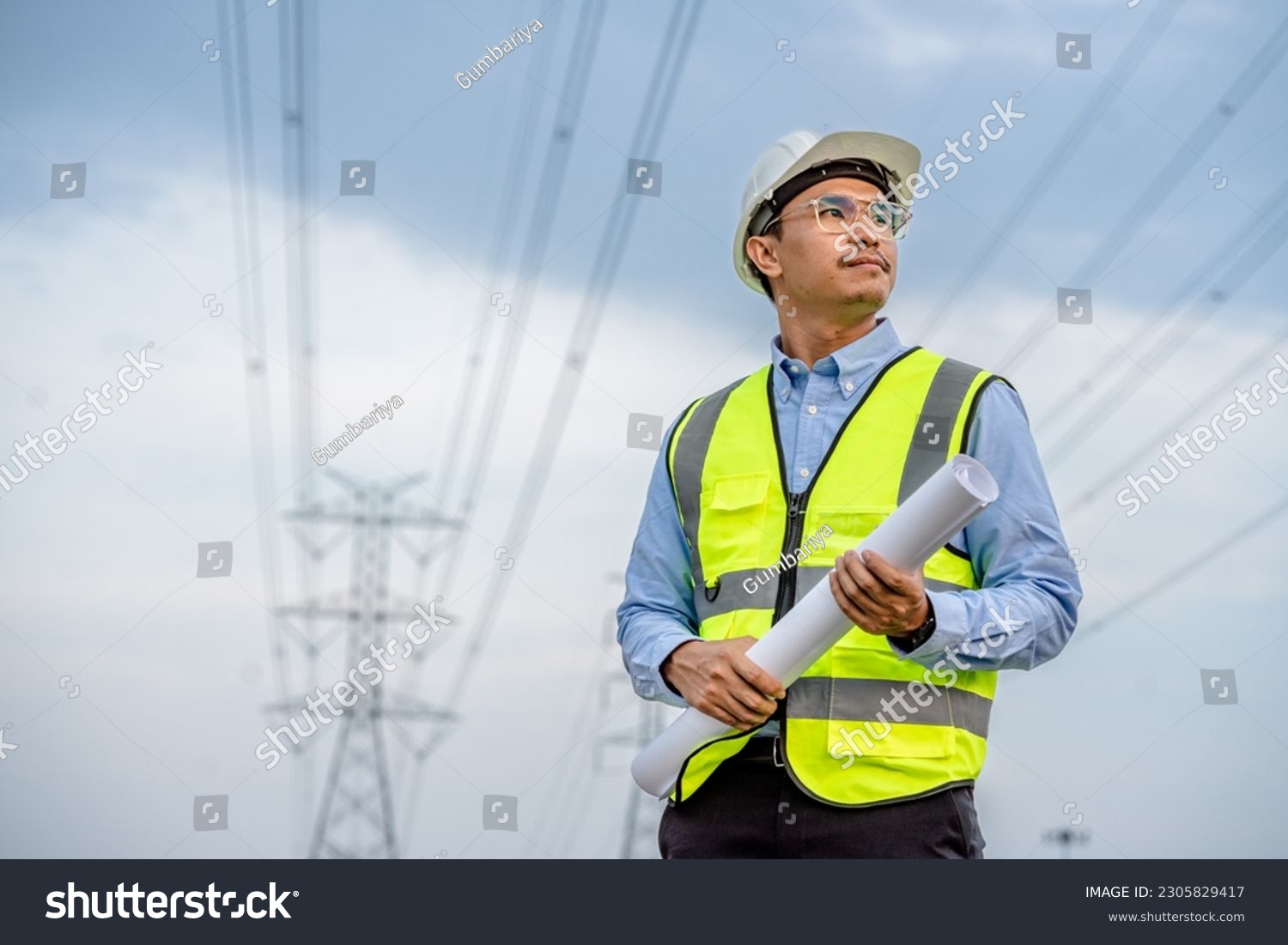 Electrical engineers holding blueprint looking confident with power line towers to project planning work producing electrical energy high voltage, energy concept. #2305829417
