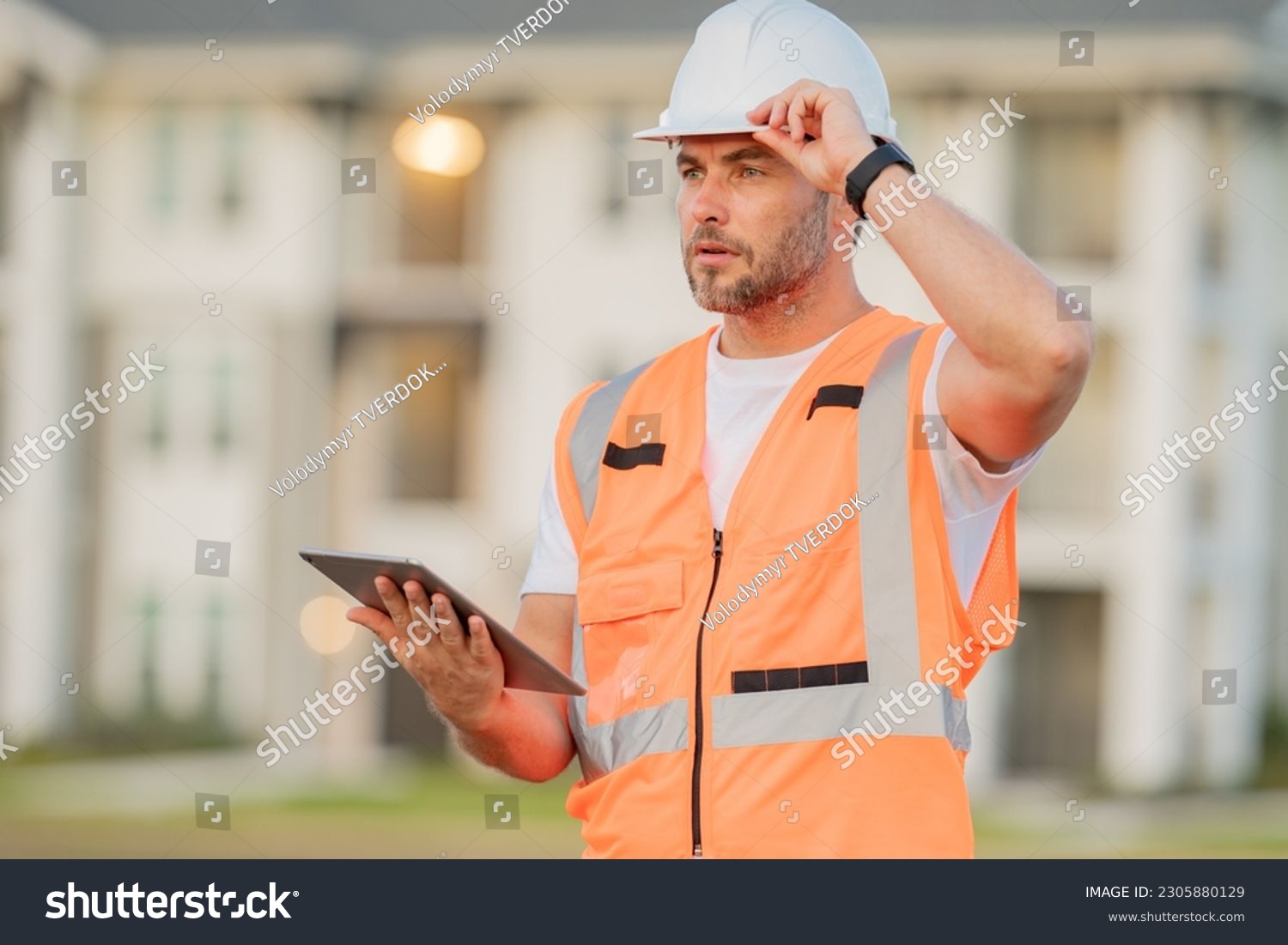 Engineer with tablet, building inspection. Builder at construction site. Buider with helmet on construction outdoor. Worker at construction site. Bilder in hardhat. #2305880129