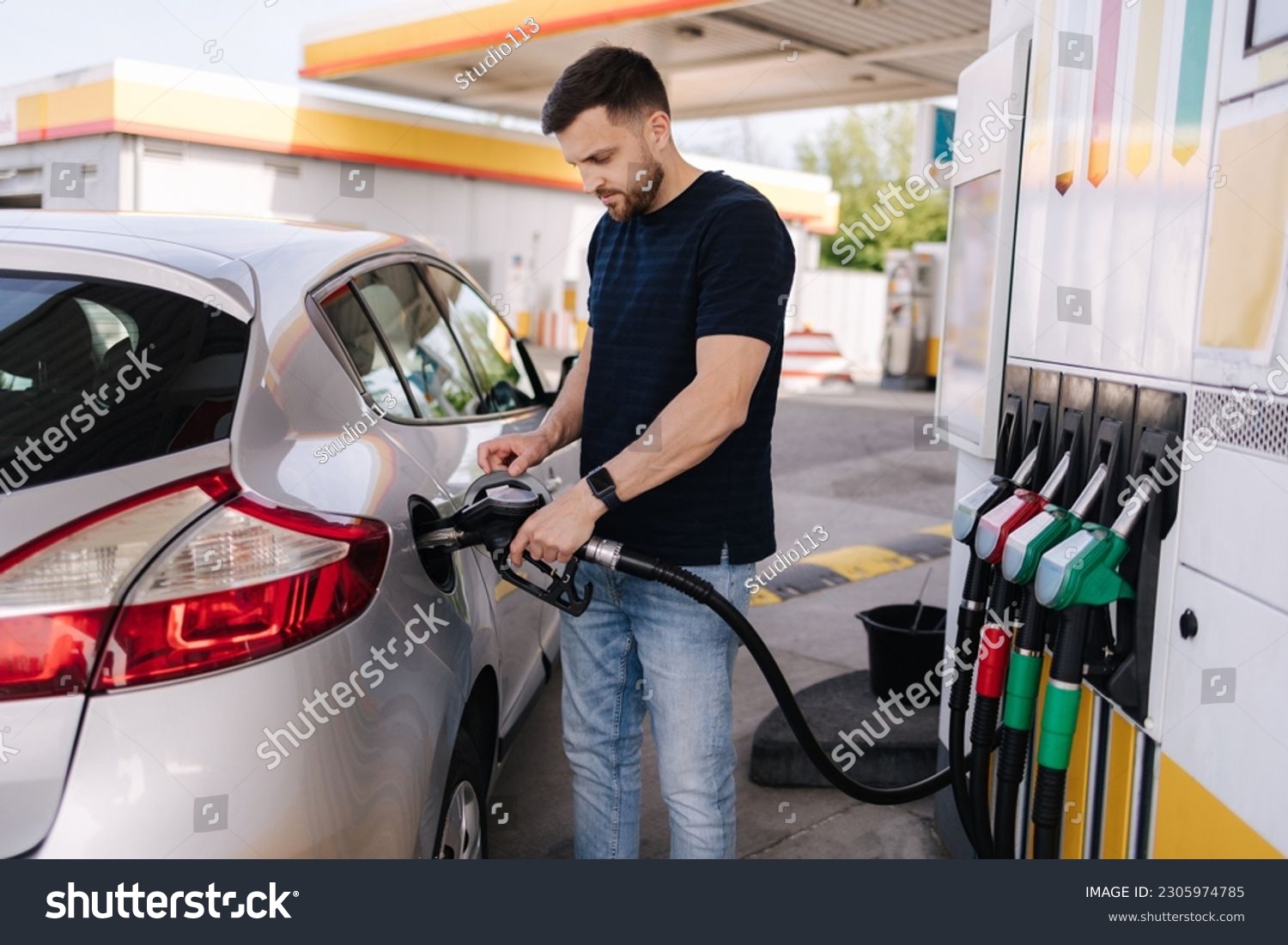Handsome young man refueling car at gas station. Male filling diesel at gasoline fuel in car using a fuel nozzle. Petrol concept. Side view #2305974785