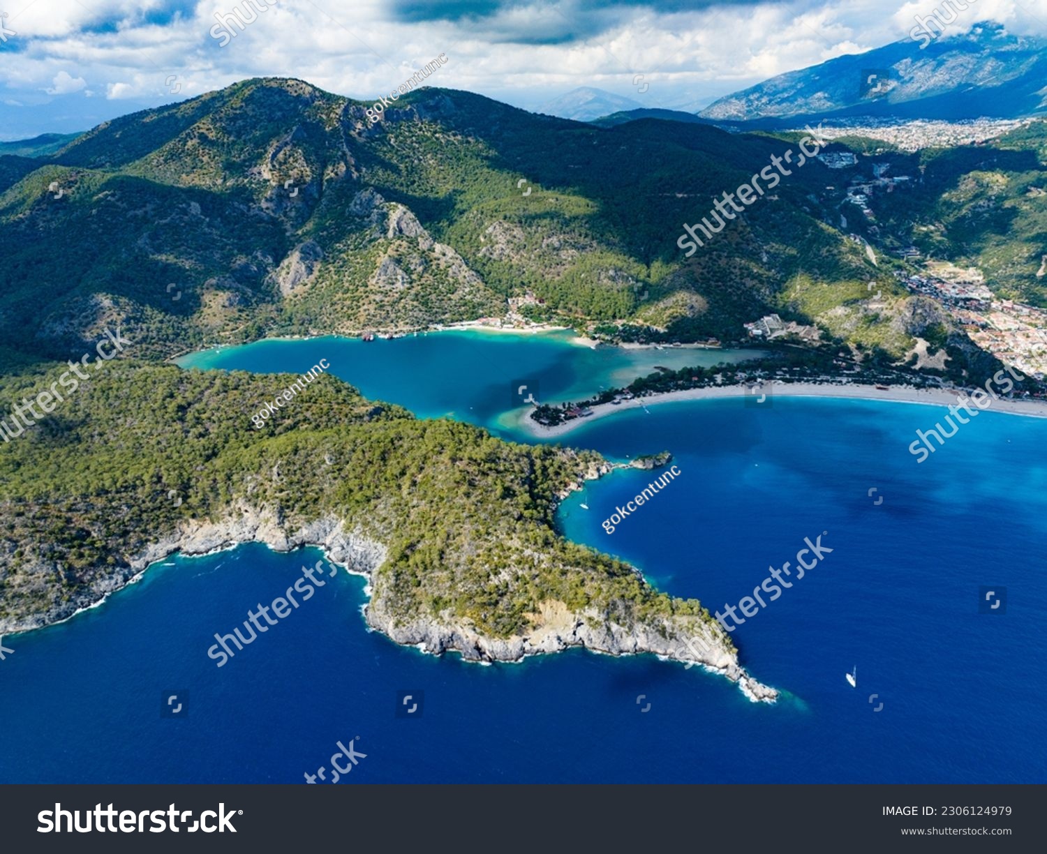 A broad view of Ölüdeniz Bay in Fethiye, Muğla, as seen from a drone. The lush mountains framing the bay enhance the scene's captivating beauty #2306124979