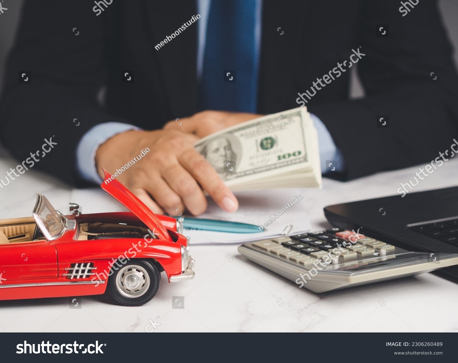 Car loan or Title loan. US dollar bills in a hand businessman while sitting at the table. Miniature a red car model, a calculator, and a laptop on a table. Car finance and insurance concept #2306260489