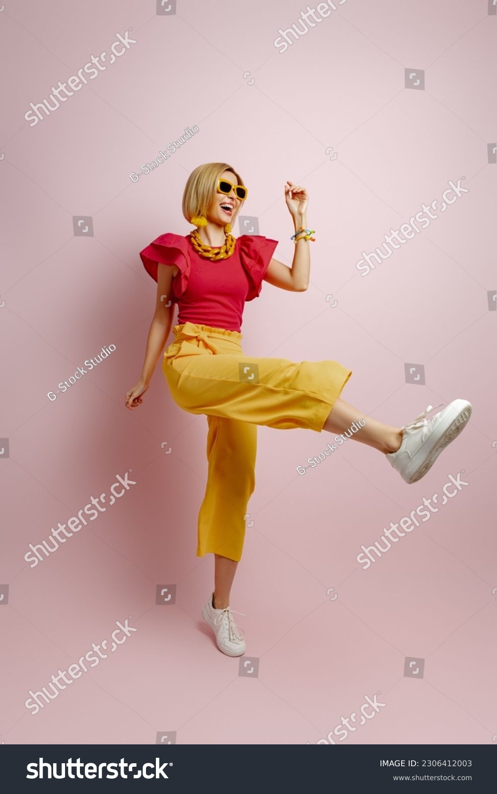 Full length of excited young woman in vibrant clothes dancing against colored background #2306412003